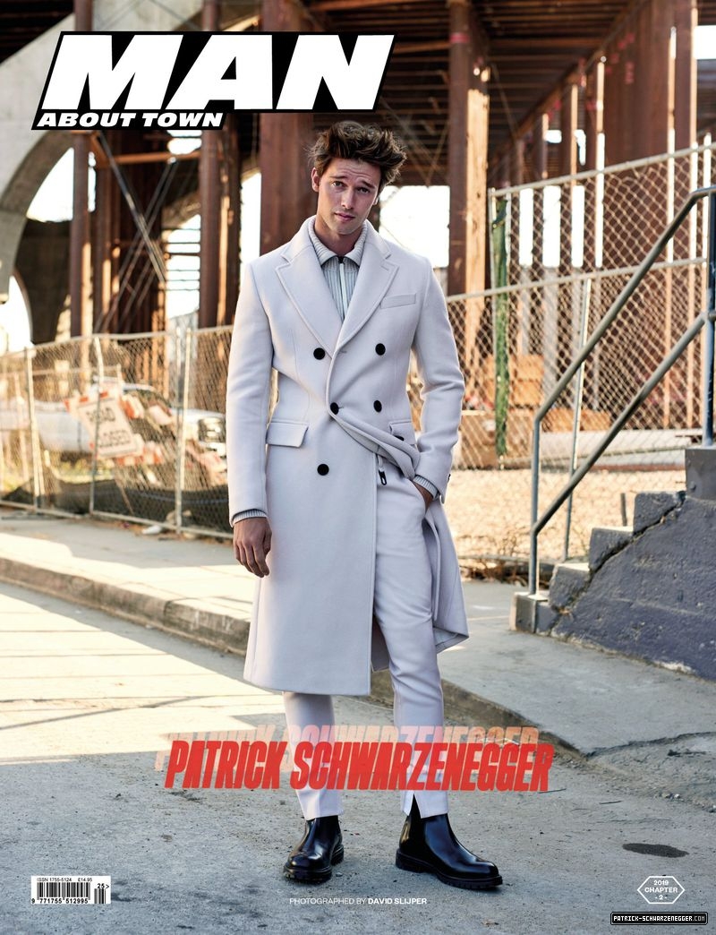 Magazine cover featuring a man in a light-colored coat and pants, standing on a city street with an industrial background and holding a magazine.