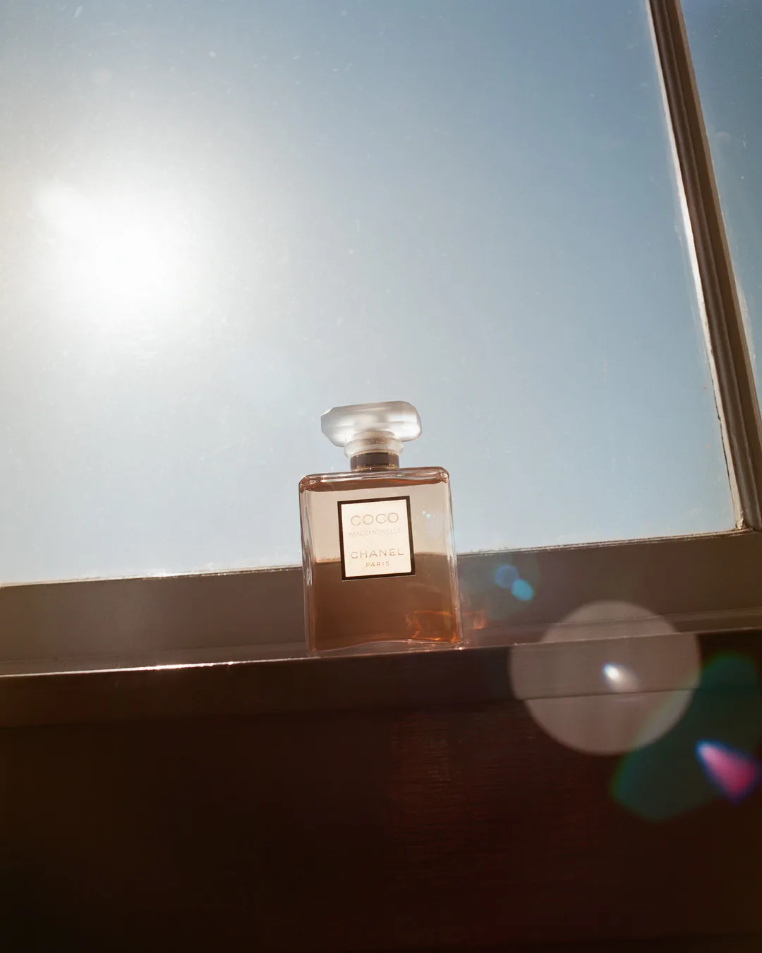 Coco Chanel perfume bottle on a shelf in front of a bright window on a sunny day with diffused lighting and lens flare.