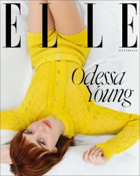 Odessa Young lying on white bedsheets wearing a vibrant yellow knitted matching top and shorts set.