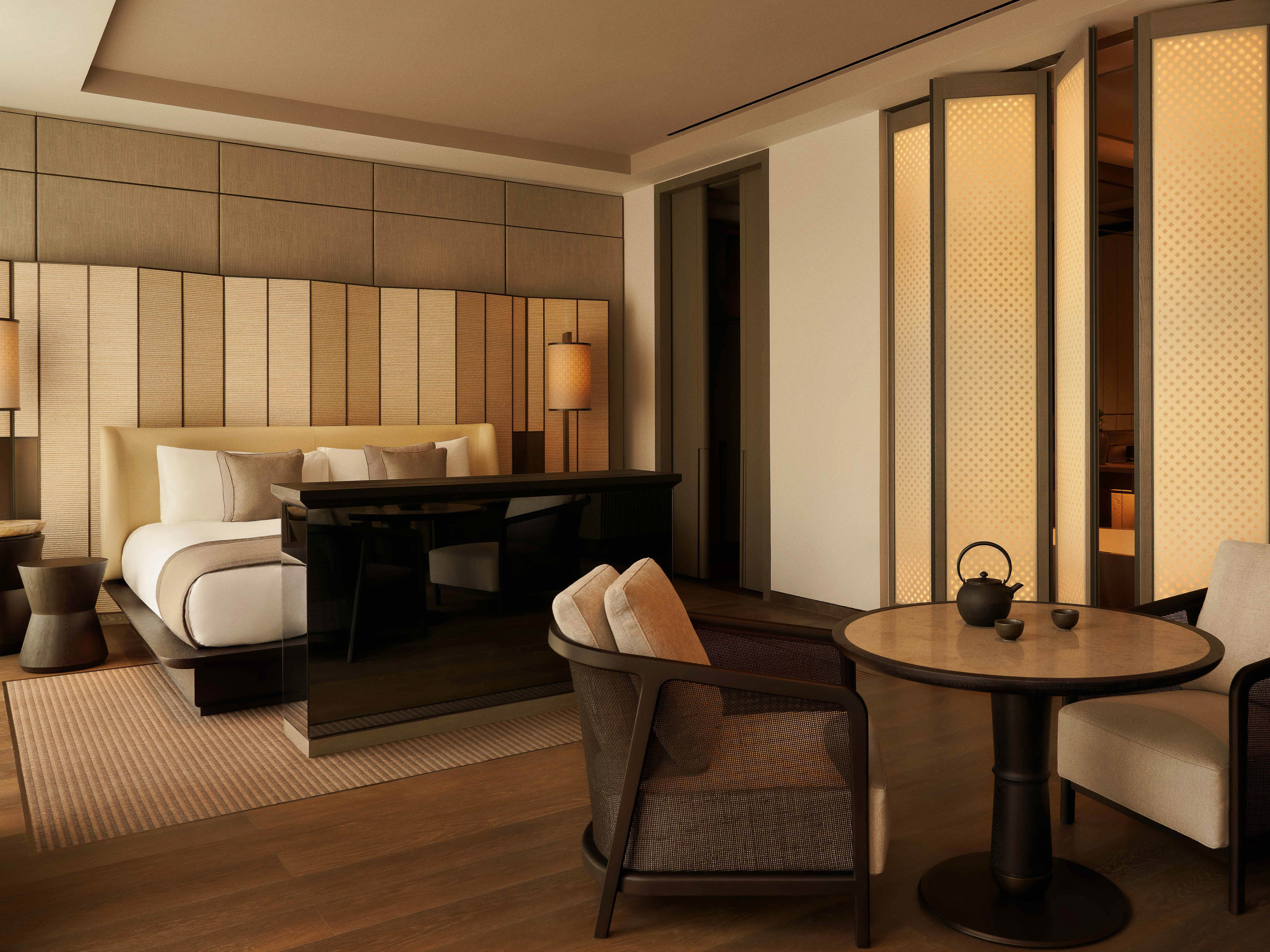 Bedroom interior featuring a bed with a headboard, a table with chairs, and decorative folding screens, creating a serene atmosphere.