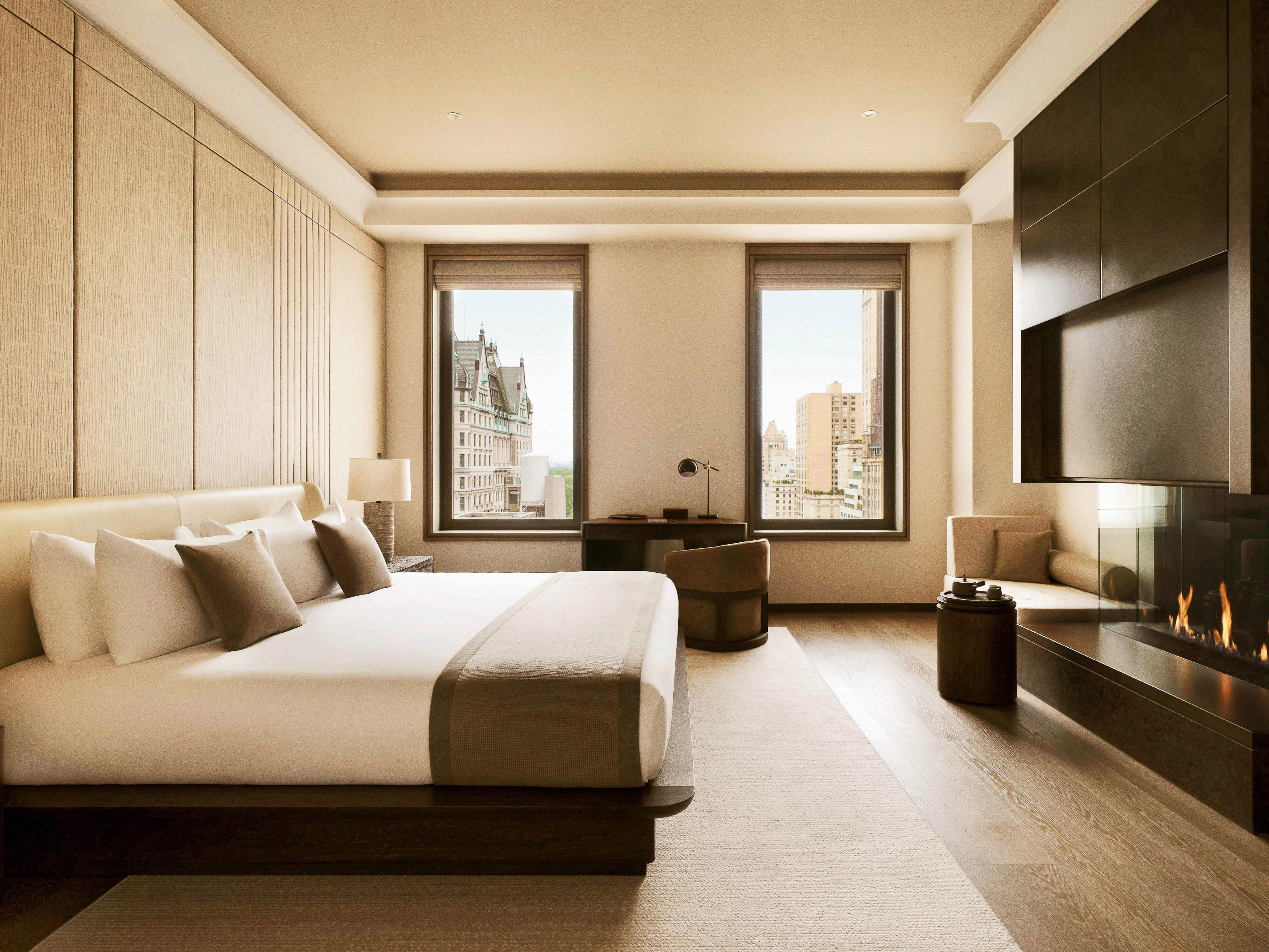 A stylish hotel room features a king-sized bed with plush pillows, a modern fireplace, a cozy window seat, and a scenic city view.