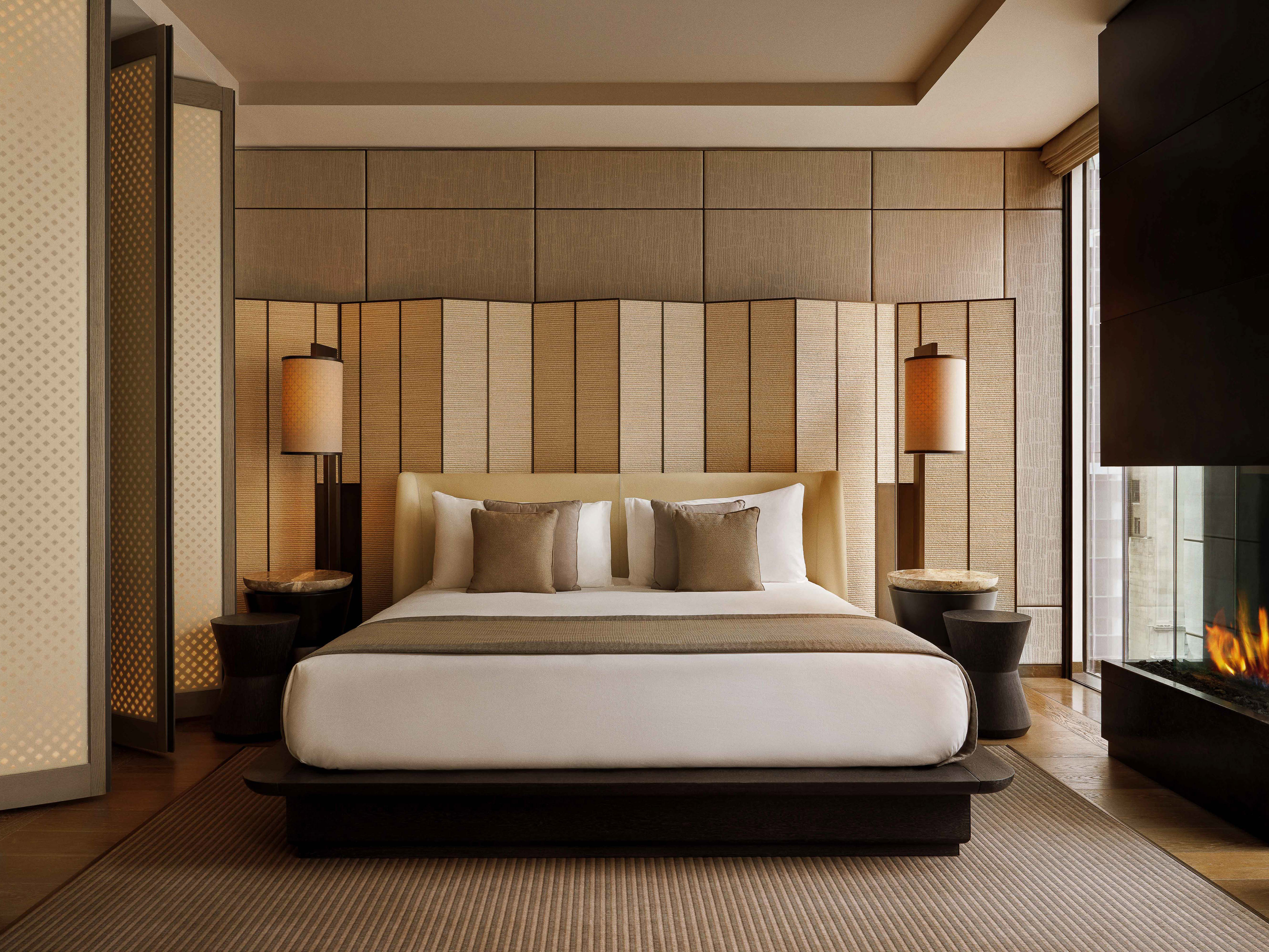 Bedroom interior featuring a king-size bed with neutral bedding, bedside tables with lamps, a fireplace, and wooden wall panels.