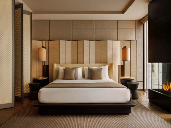 Bedroom interior featuring a king-size bed with neutral bedding, bedside tables with lamps, a fireplace, and wooden wall panels.