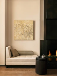 Minimalist beige daybed with cushions beside a contemporary fireplace and a small dark side table holding a ceramic tea set.