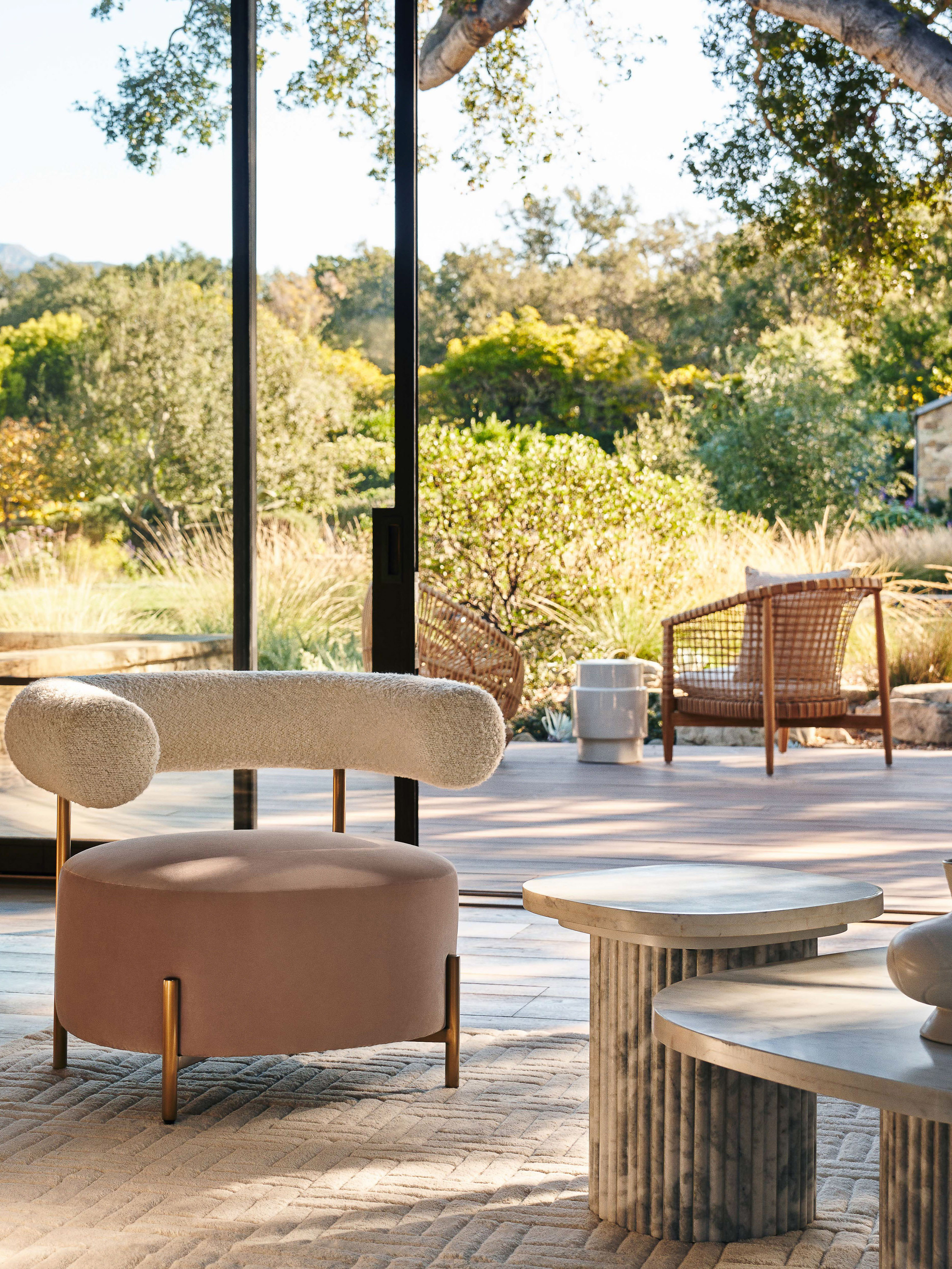 Indoor living room with modern furniture including a velvet-upholstered accent chair, stone coffee table, and a view to outdoor greenery.