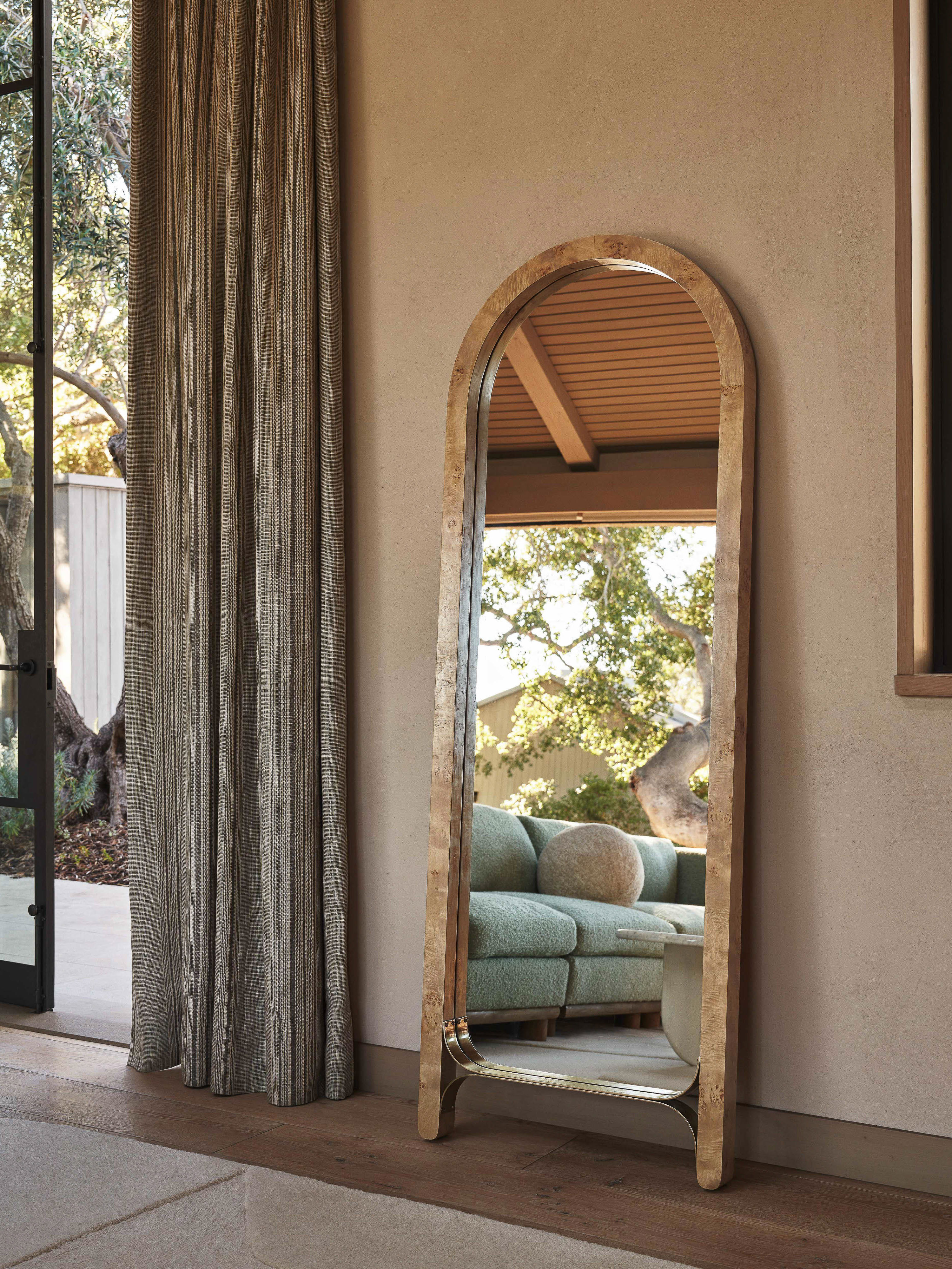 Interior view featuring a full-length arched mirror reflecting a living room with a sofa, hardwood floors, and natural light through a window.