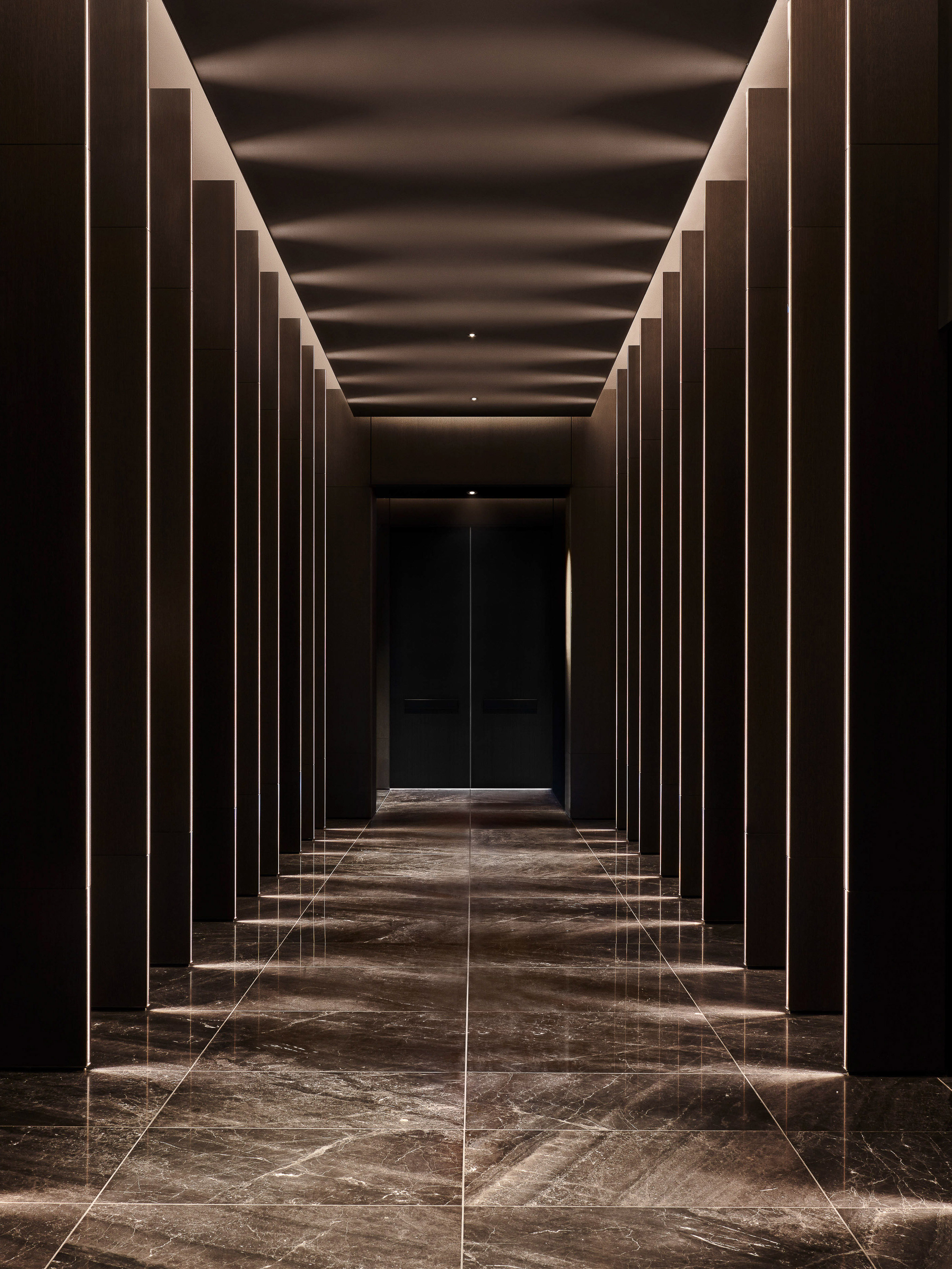 Architectural interior view of a hallway with vertically paneled walls, tile floor, and recessed lighting creating a symmetrical perspective.