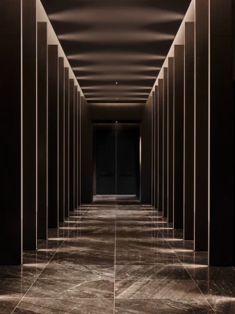 Architectural interior view of a hallway with vertically paneled walls, tile floor, and recessed lighting creating a symmetrical perspective.