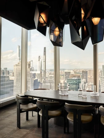 Dining room features a long oval table, geometric chandelier, and a backdrop of New York City skyline through large windows.