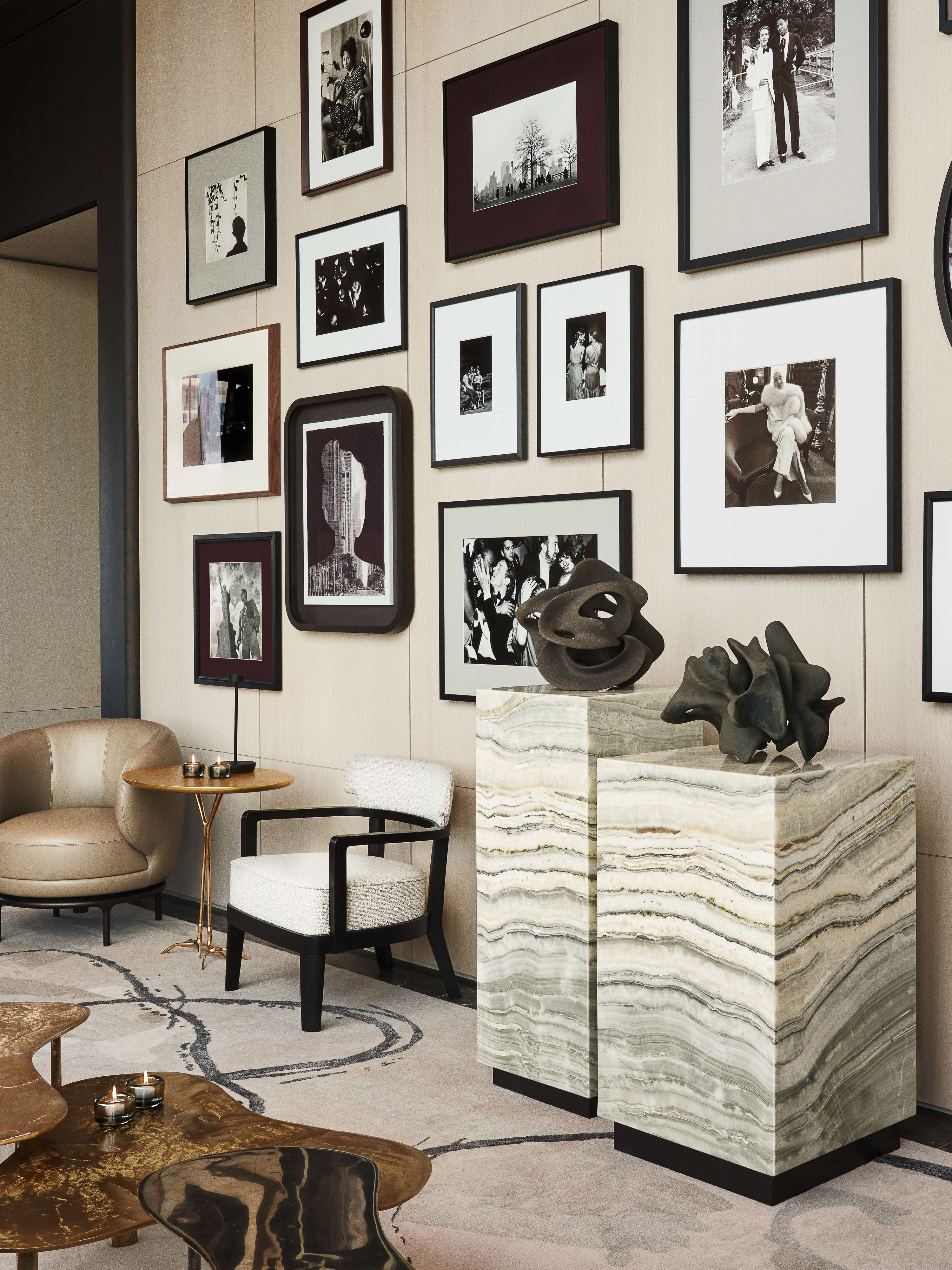 Interior view of a modern living room featuring marble side tables, neutral-toned chairs, and a gallery wall with framed black-and-white prints.