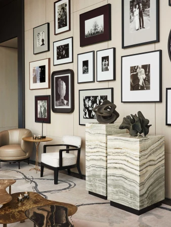 Interior view of a modern living room featuring marble side tables, neutral-toned chairs, and a gallery wall with framed black-and-white prints.