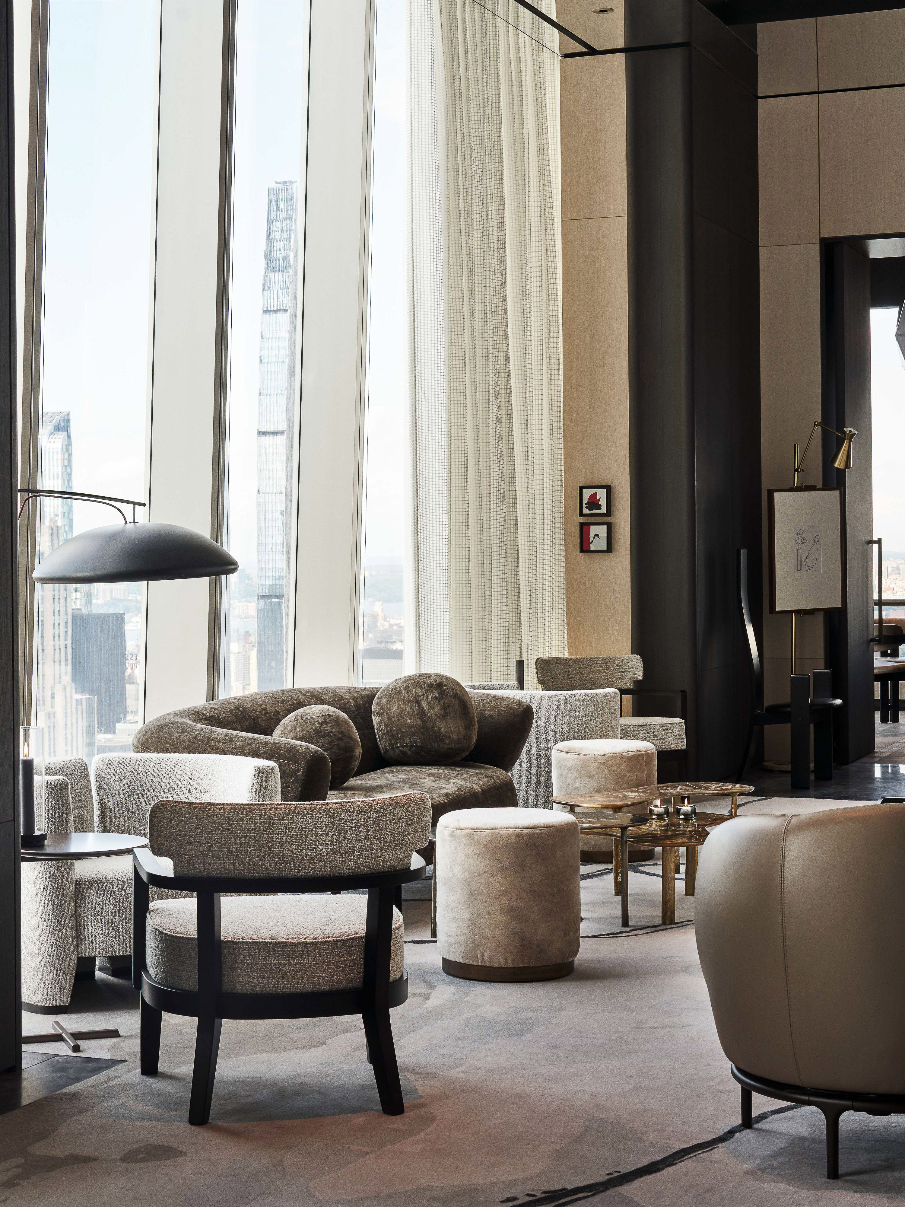Living room interior showcasing a curved sofa, armchairs, stools, and expansive windows with a city view, creating a modern and stylish space.