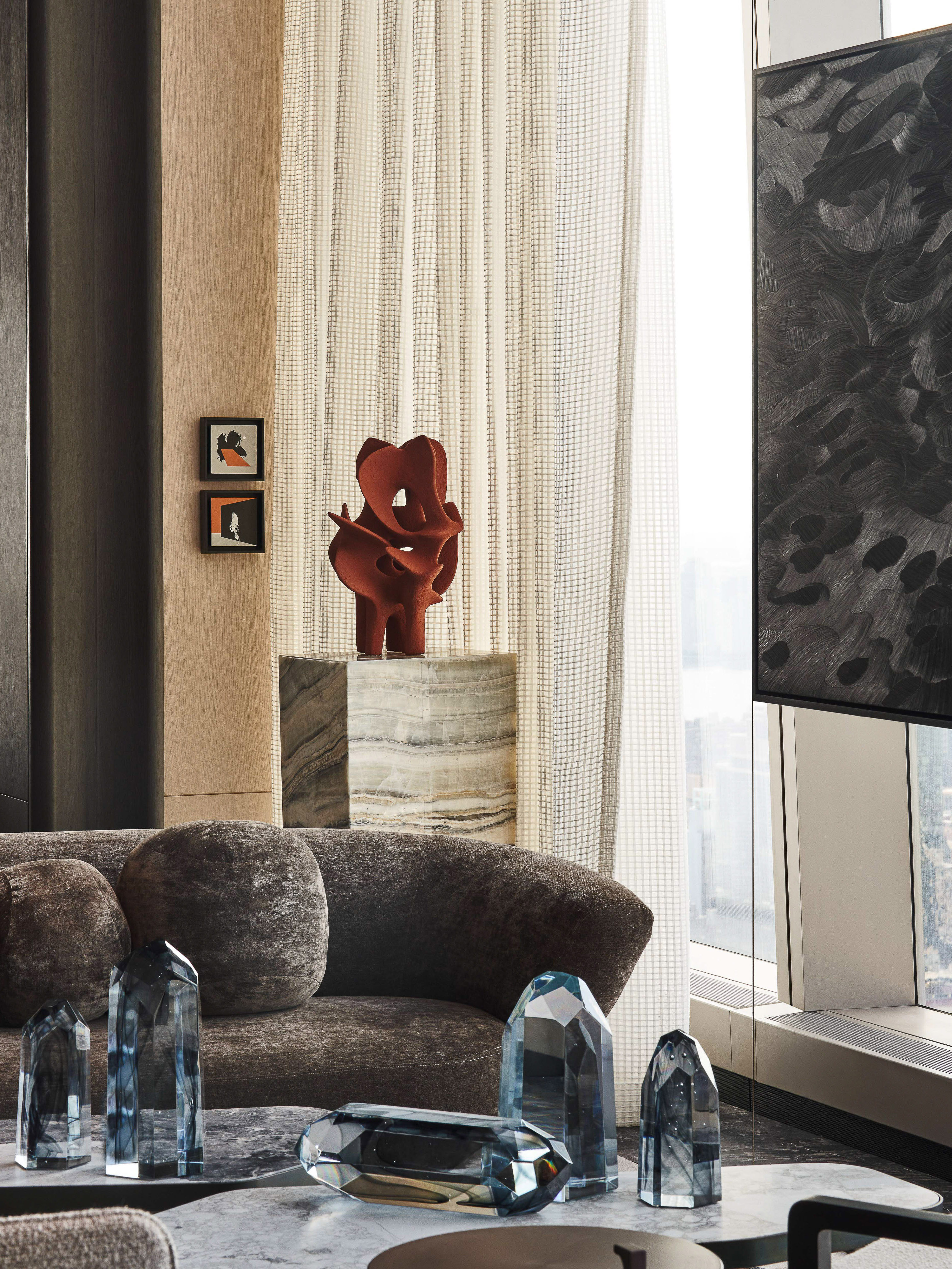 Modern interior showcasing gray sofa, glass sculptures, and abstract art on a marble plinth, bathed in soft, diffused lighting.