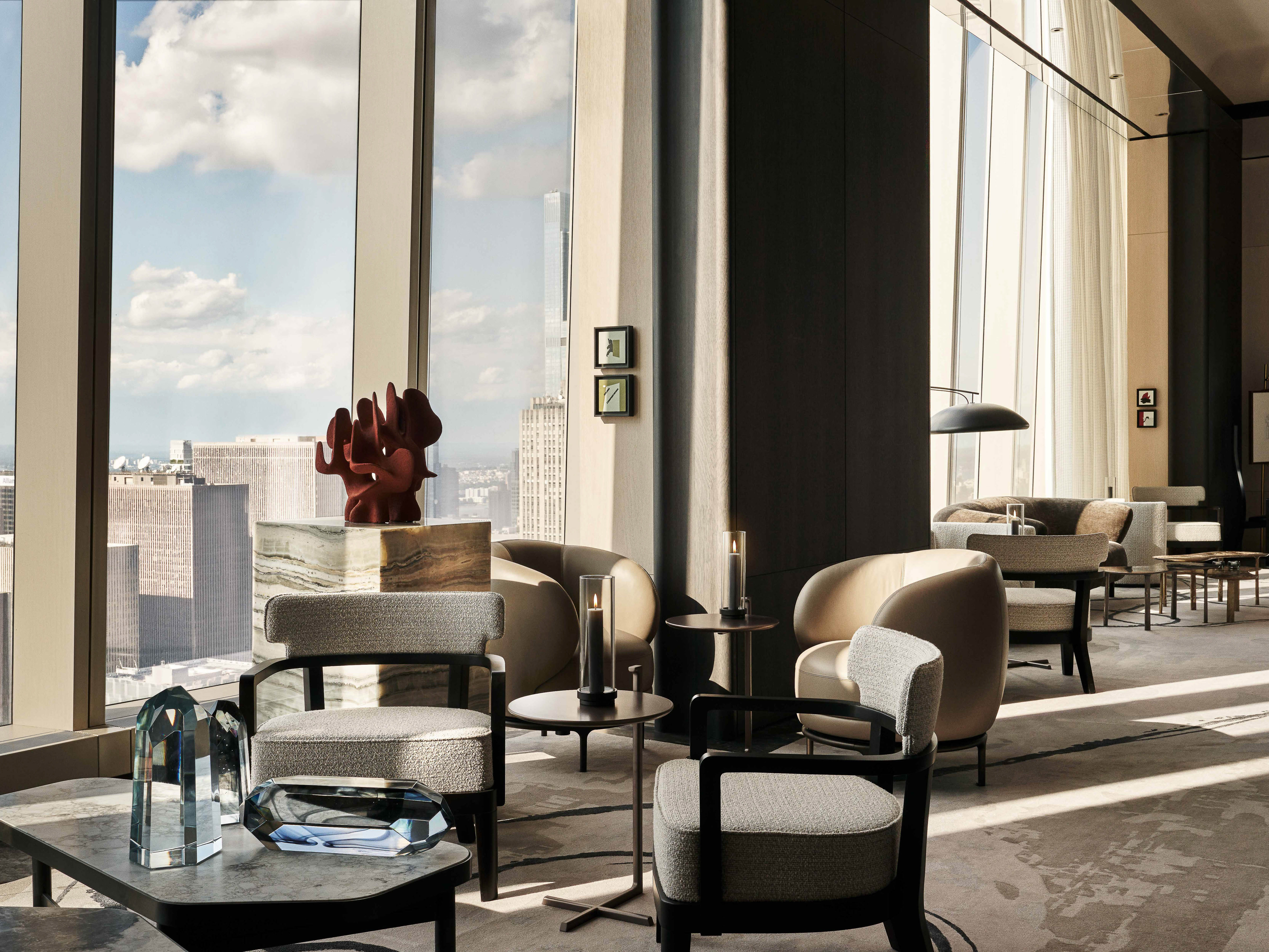 Modern lounge with seating, tables, decorative glass objects, and a cityscape view through large windows, creating a serene atmosphere.