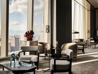 Modern luxury high-rise lounge with contemporary armchairs, coffee tables, and floor-to-ceiling windows overlooking a city skyline.