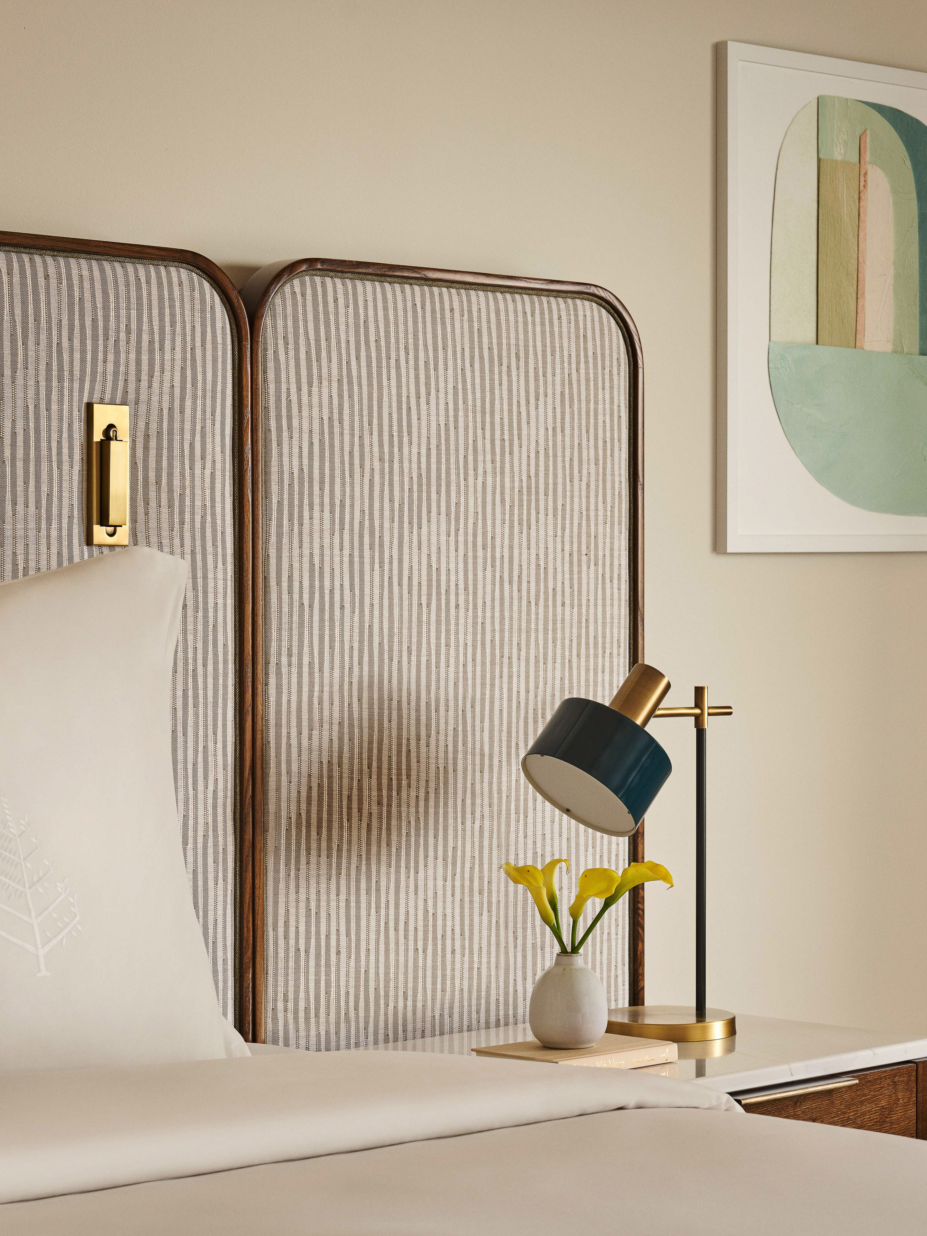 Interior shot of bedroom: upholstered headboard, lamp with yellow flowers on nightstand, and abstract art on the wall create inviting space.