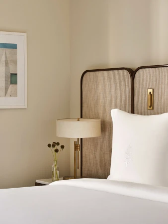 Bedroom interior featuring a bed with white linens, a textured headboard, bedside table with a lamp, and framed wall art in a neutral color palette.