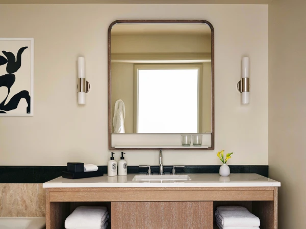 Bathroom interior with a wooden vanity, white countertop, mirror, wall-mounted sconces, and a framed abstract art piece on the wall.