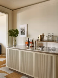 Fluted beige credenza styled with liquor bottles, glassware, and a monstera leaf in a luxury Four Seasons hotel room.