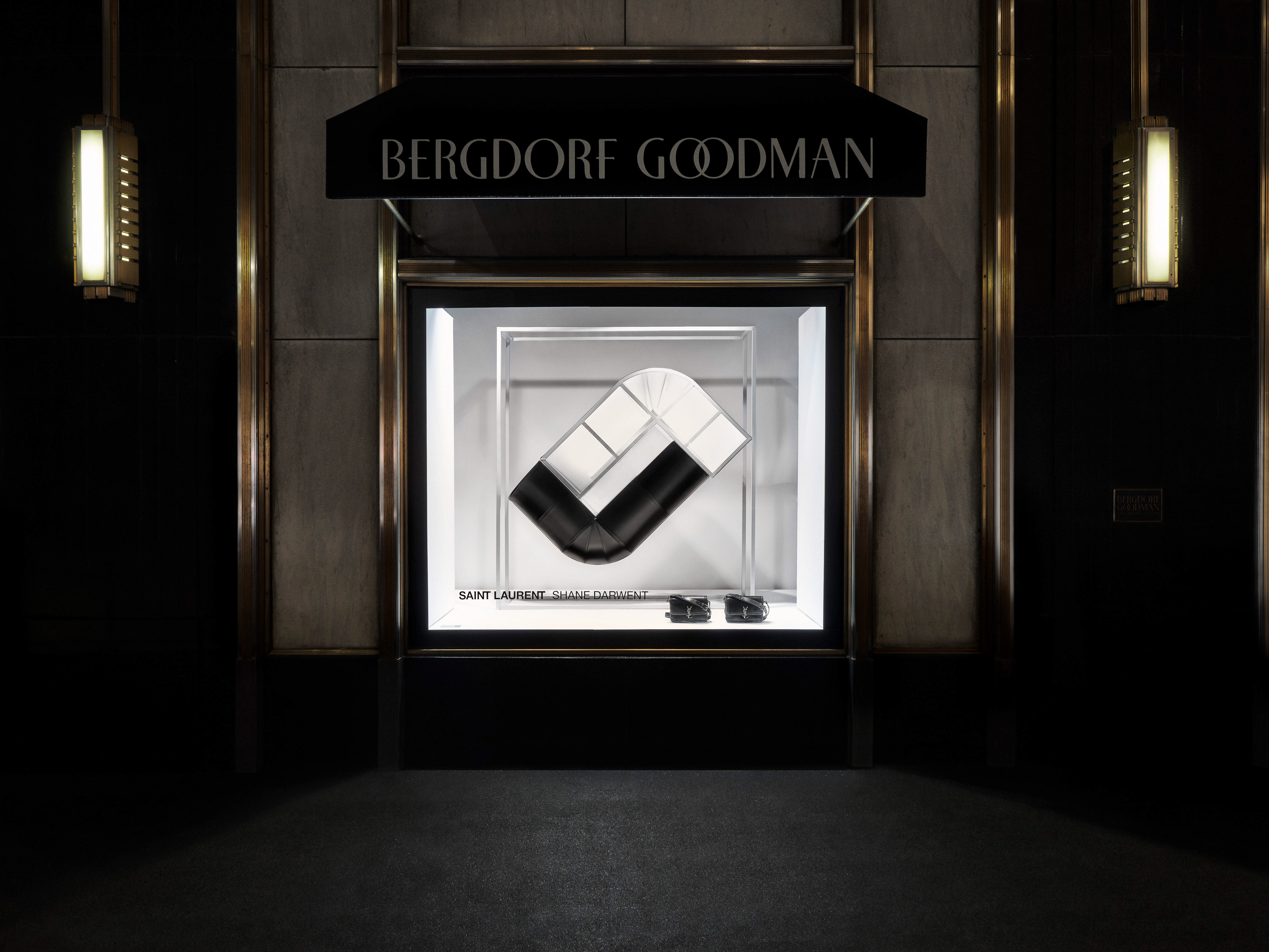 A storefront display for Bergdorf Goodman featuring a black and white handbag on a stand, lit by overhead lighting and framed by architectural details.