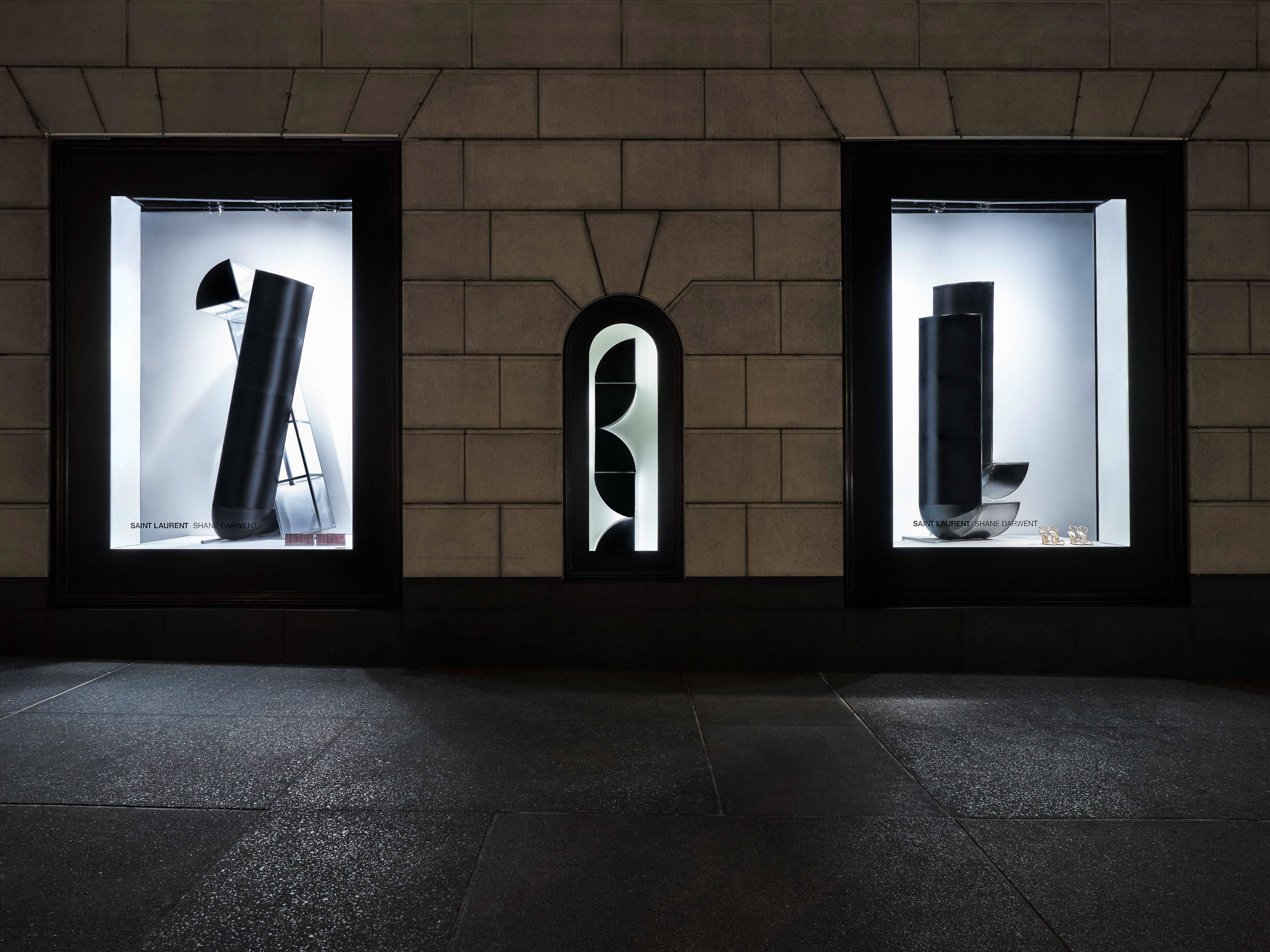 View of a Saint Laurent store window display with abstract black objects and jewelry on display; modern fashion advertisement.