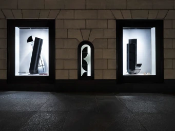Illuminated Saint Laurent storefront display windows featuring black geometric sculptures set into a stone block facade at night.