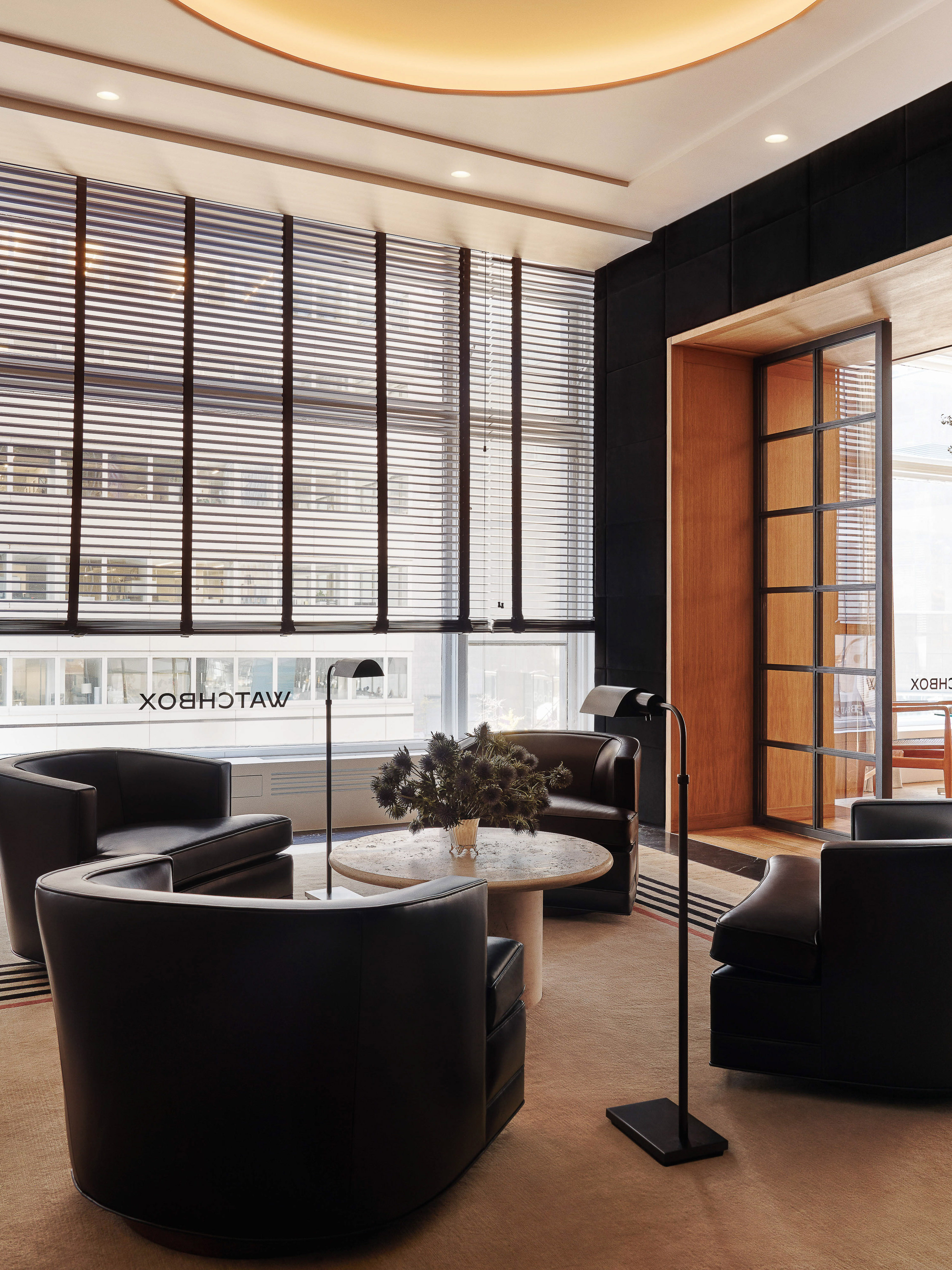 Contemporary interior design of a waiting room with leather chairs, floor lamps, a coffee table, and window blinds in a stylish room.
