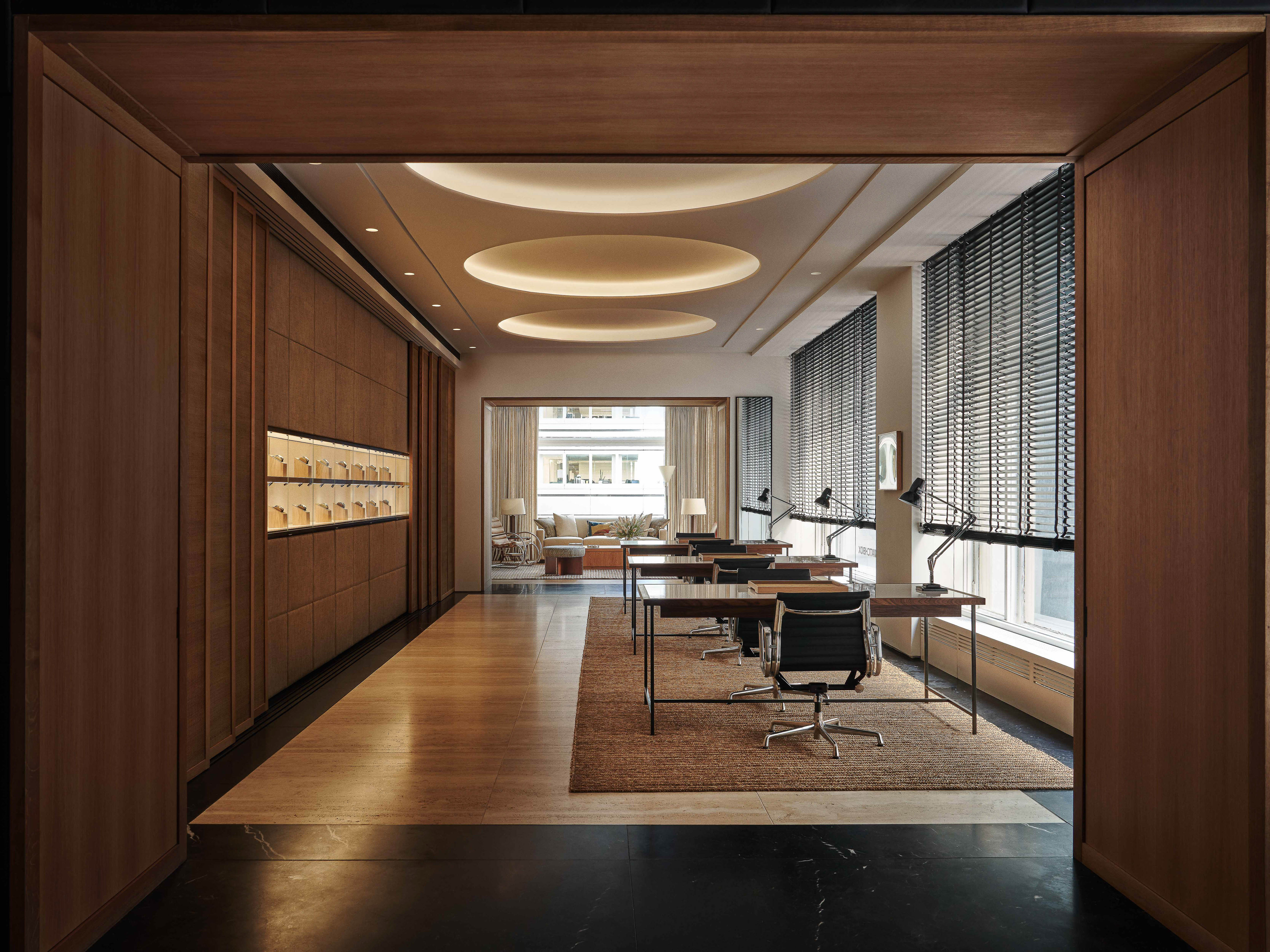 Modern office interior with wooden floors, tables and black chairs, featuring indirect ceiling lights and window blinds.