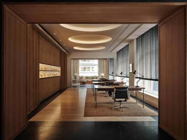 Modern office interior with wooden floors, tables and black chairs, featuring indirect ceiling lights and window blinds.