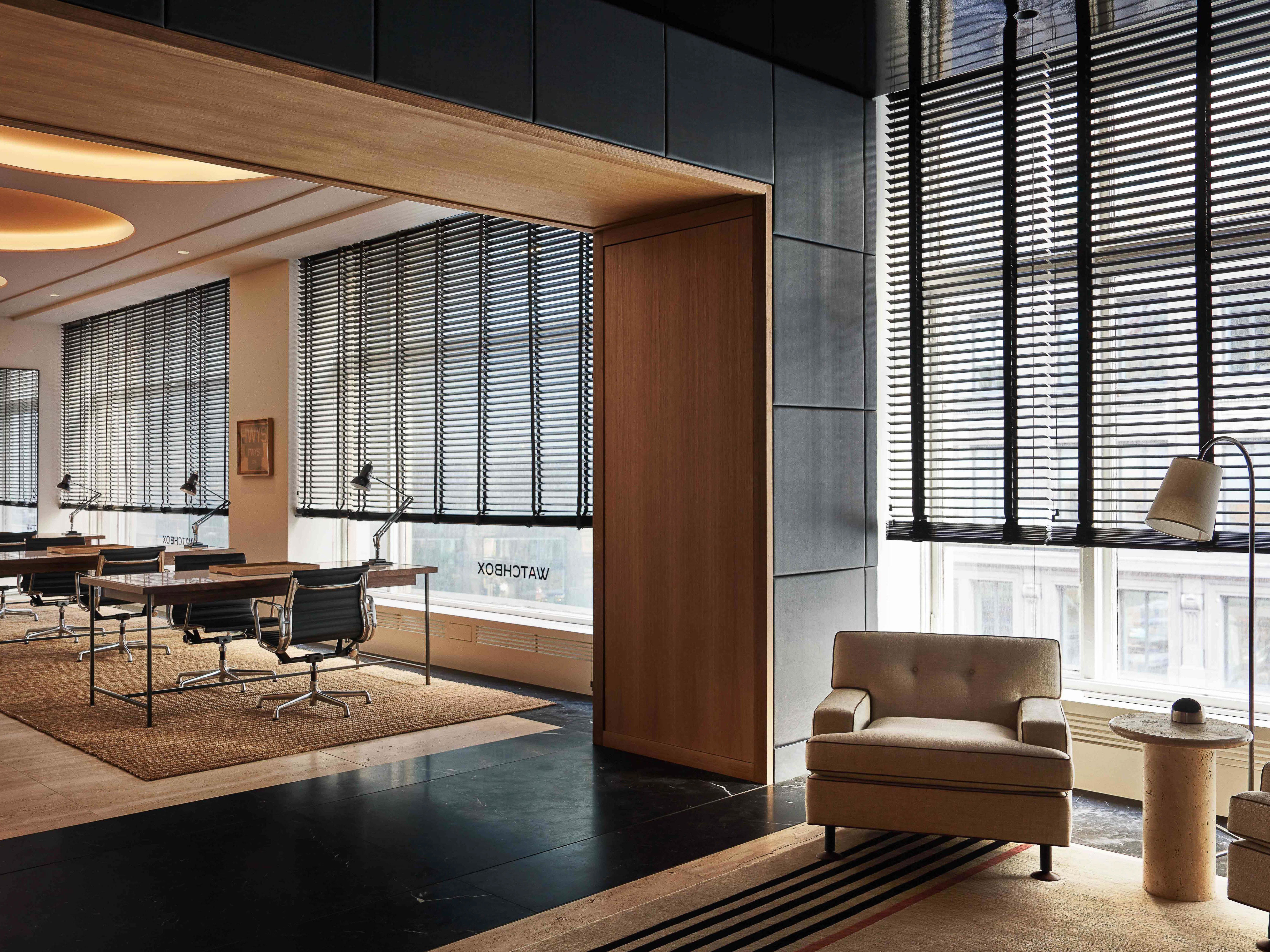 Modern office interior featuring an armchair, window with blinds, desk with chair, and contemporary furniture, bathed in soft, ambient light.