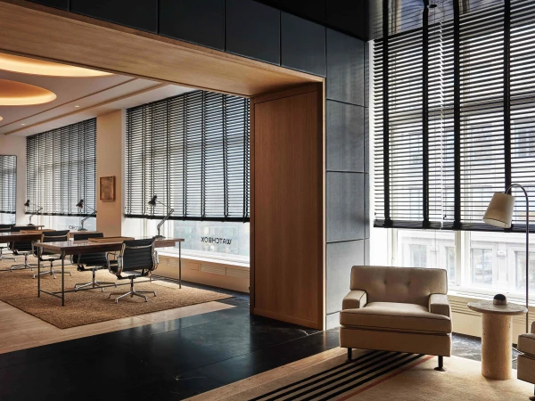 Modern office interior featuring an armchair, window with blinds, desk with chair, and contemporary furniture, bathed in soft, ambient light.