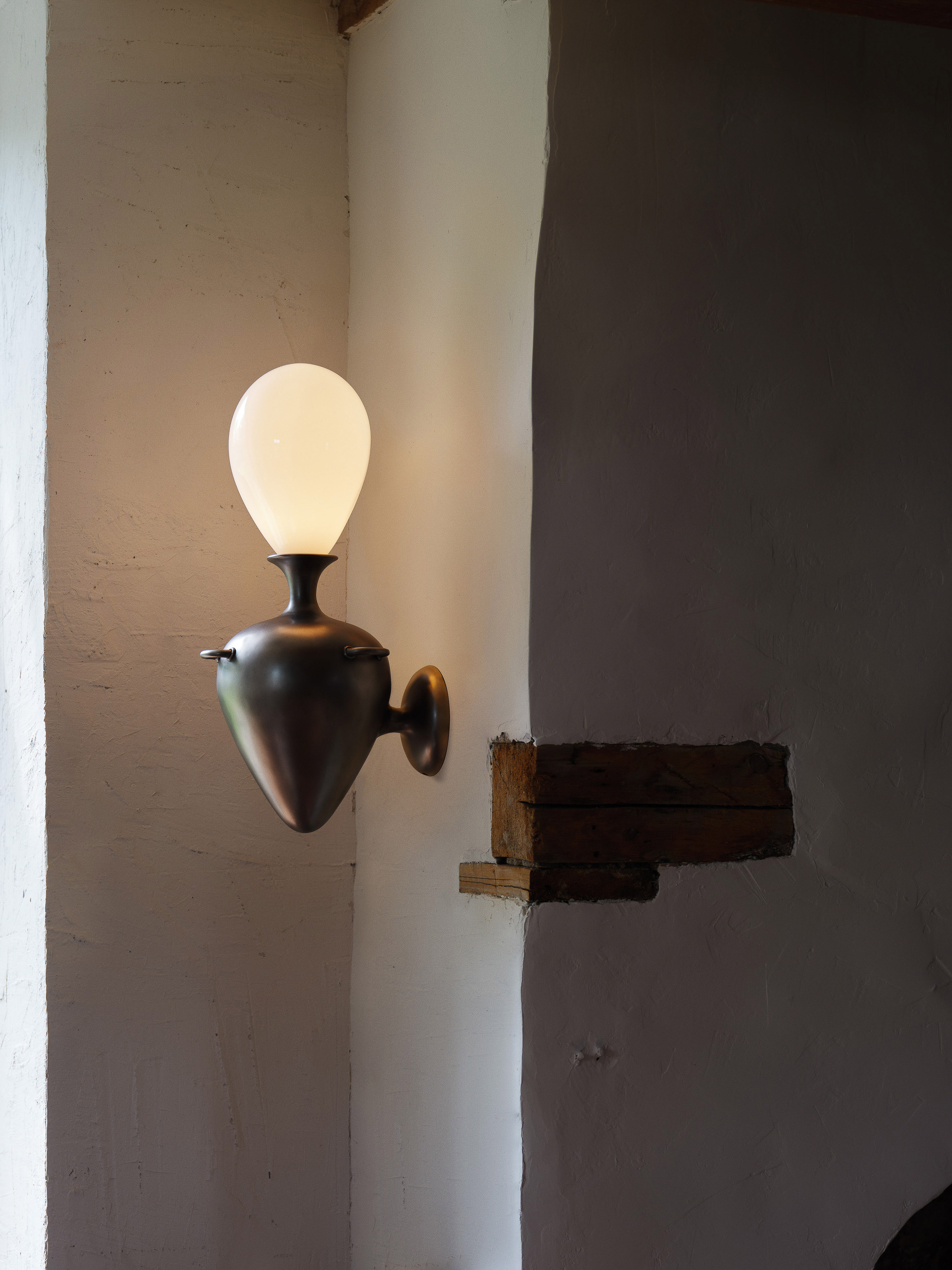 Wall sconce lighting fixture with a pear-shaped shade casts a warm glow against a textured off-white wall in an indoor setting.