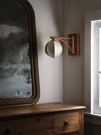Indoor room scene with an antique wood dresser, an aged mirror, and a decorative wall-mounted light fixture with a round fabric shade.