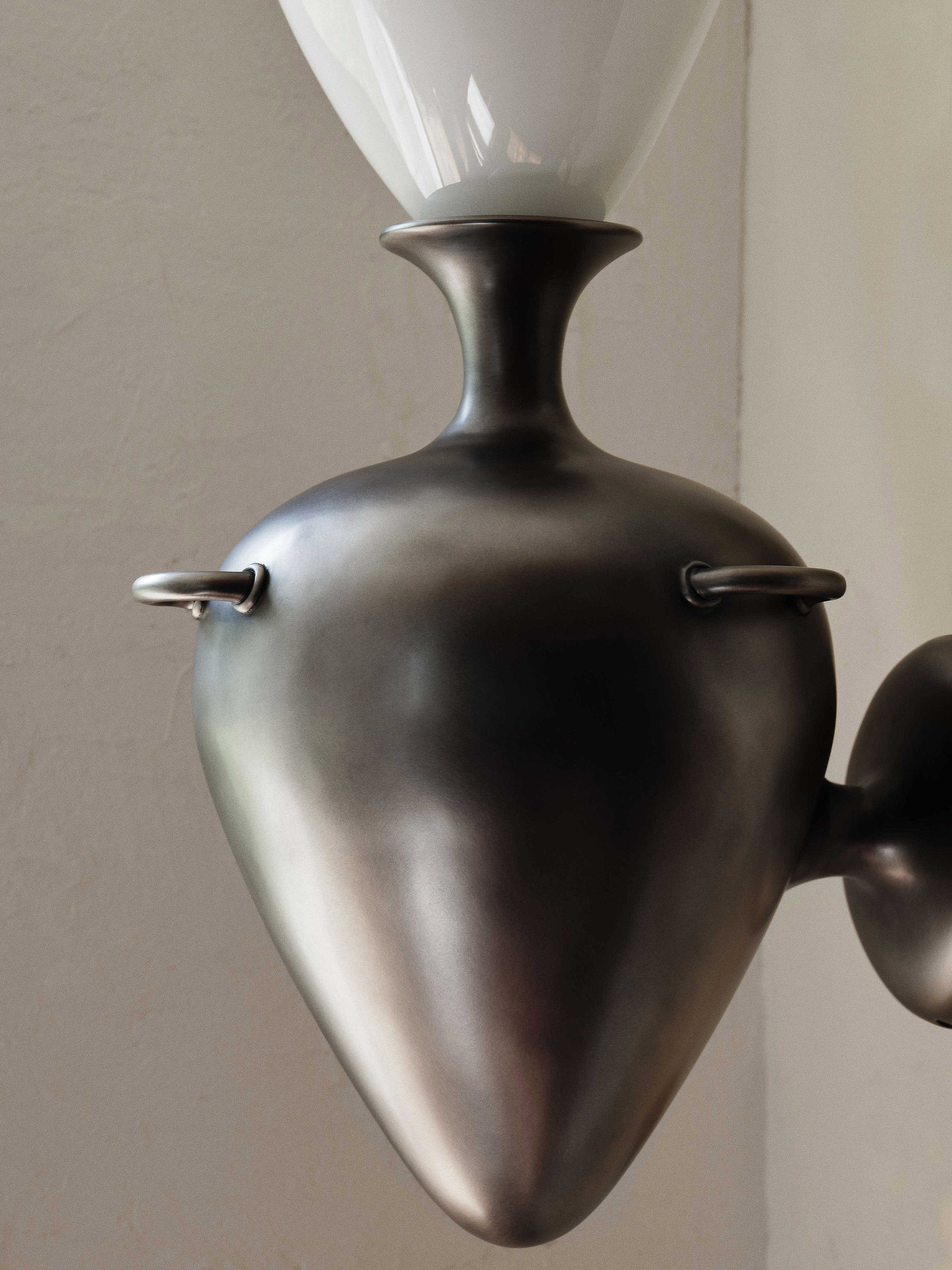 Modern interior lighting fixture featuring a gray metal frame and a white glass shade in an indoor setting, casting soft light.