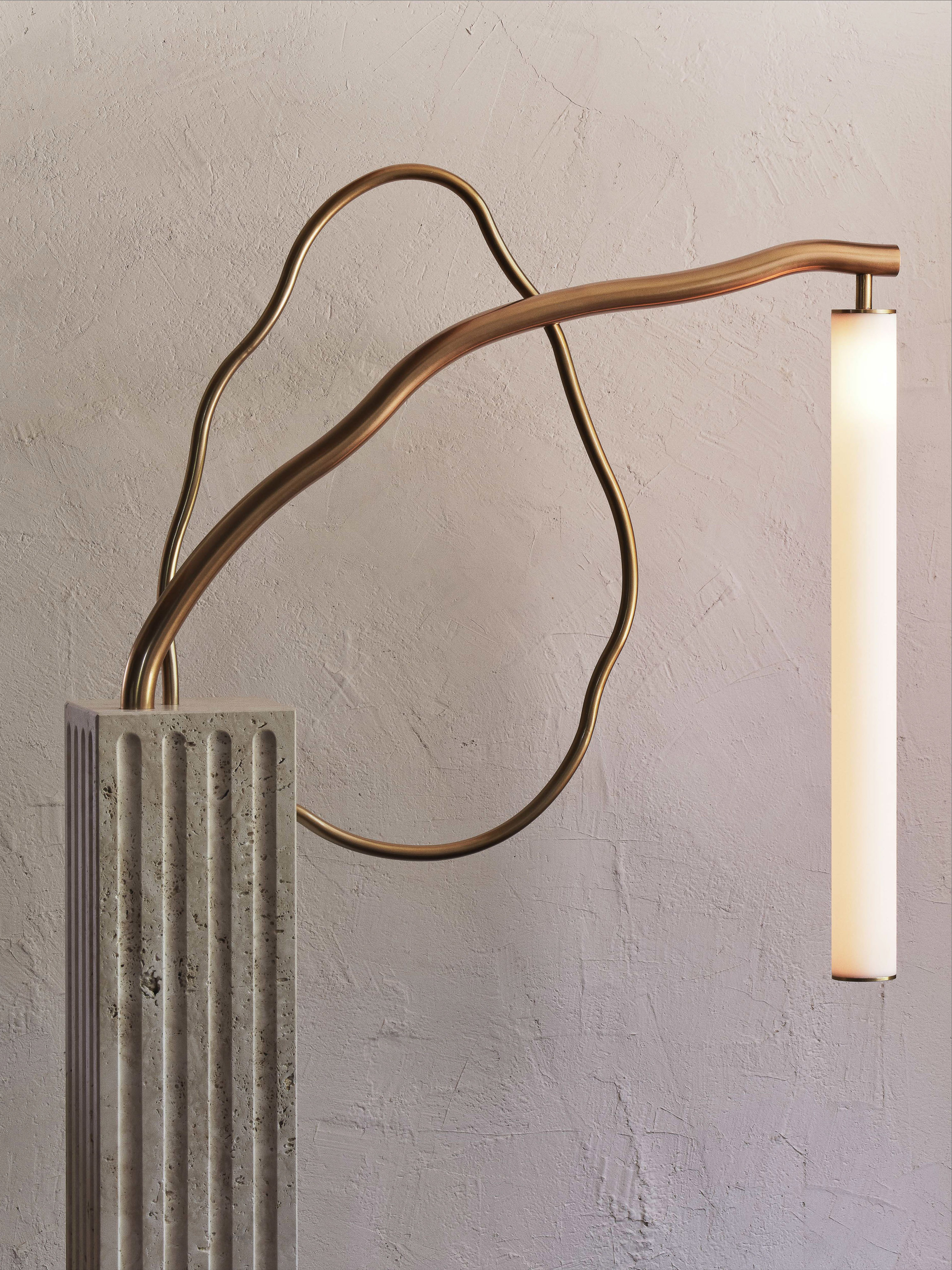 Contemporary floor lamp features a cylindrical light shade, a metal arm, and a fluted stone base against a textured wall.