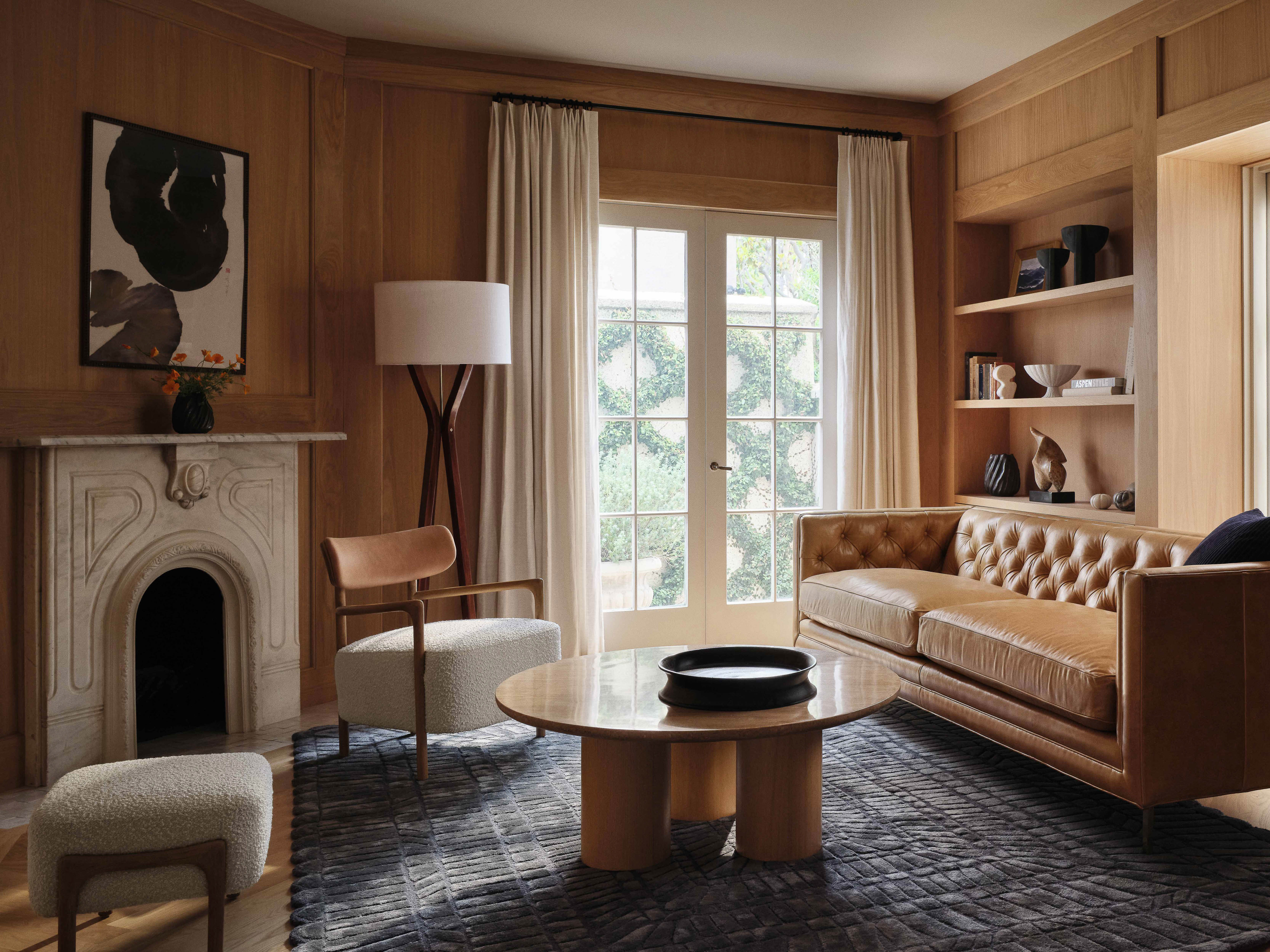 Living room interior with a leather sofa, marble fireplace, round coffee table, and natural light from a large window.