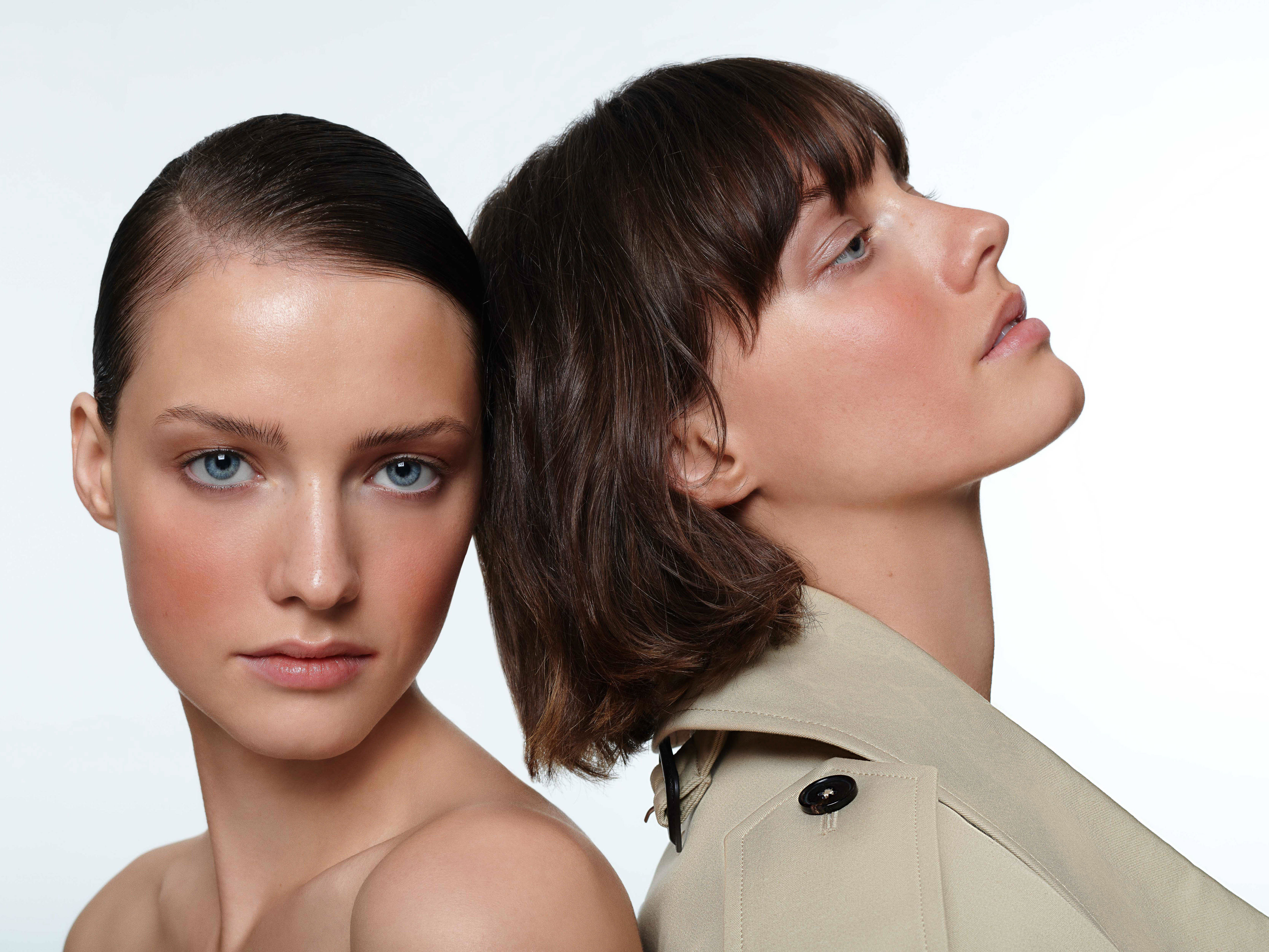 Close-up portrait of two women with natural makeup and stylish haircuts in a bright studio setting, showcasing beauty and fashion.