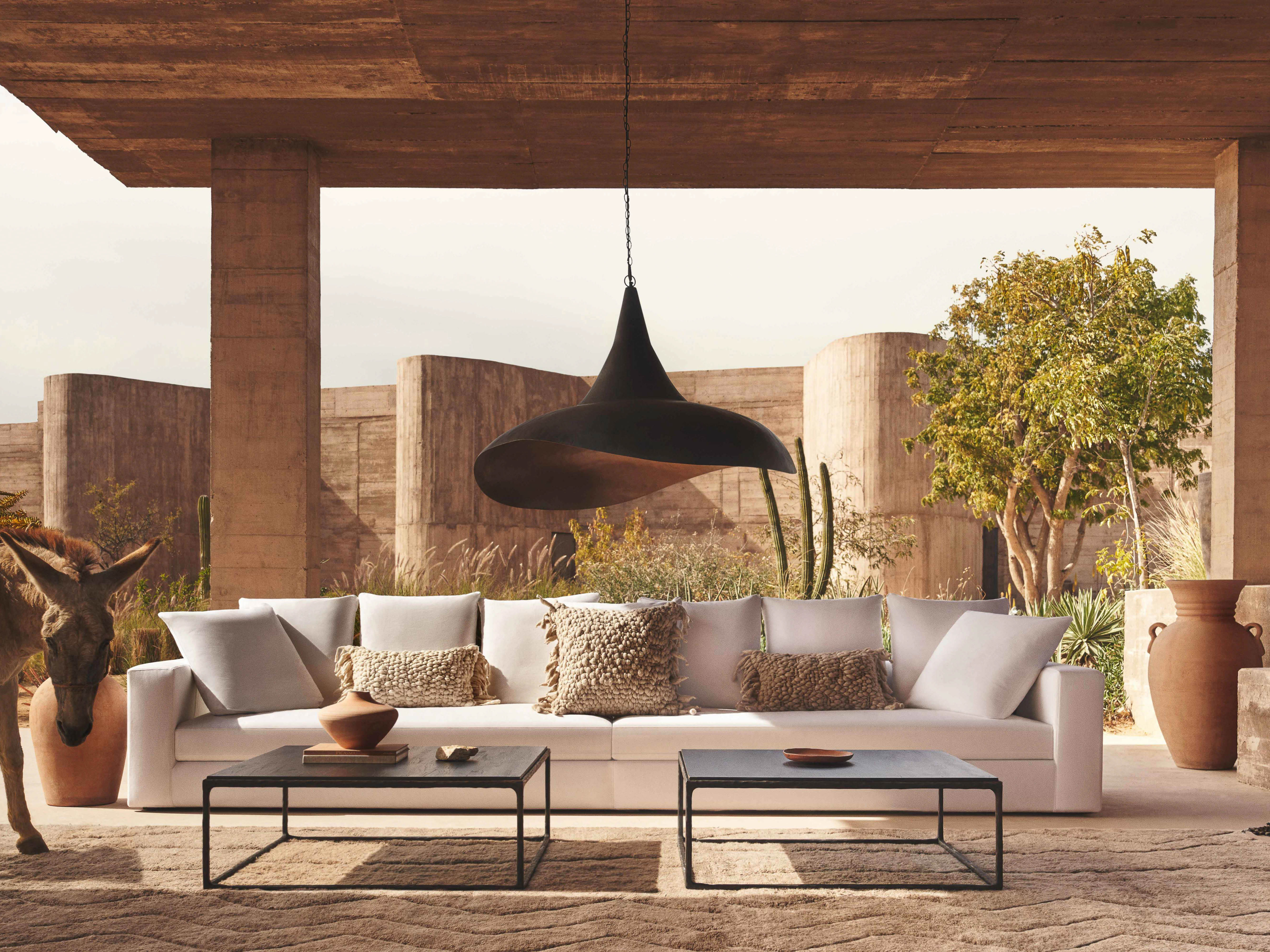 Outdoor living space showcases a modern white sofa with throw pillows, a dark coffee table, and minimalist decor, under a concrete structure.