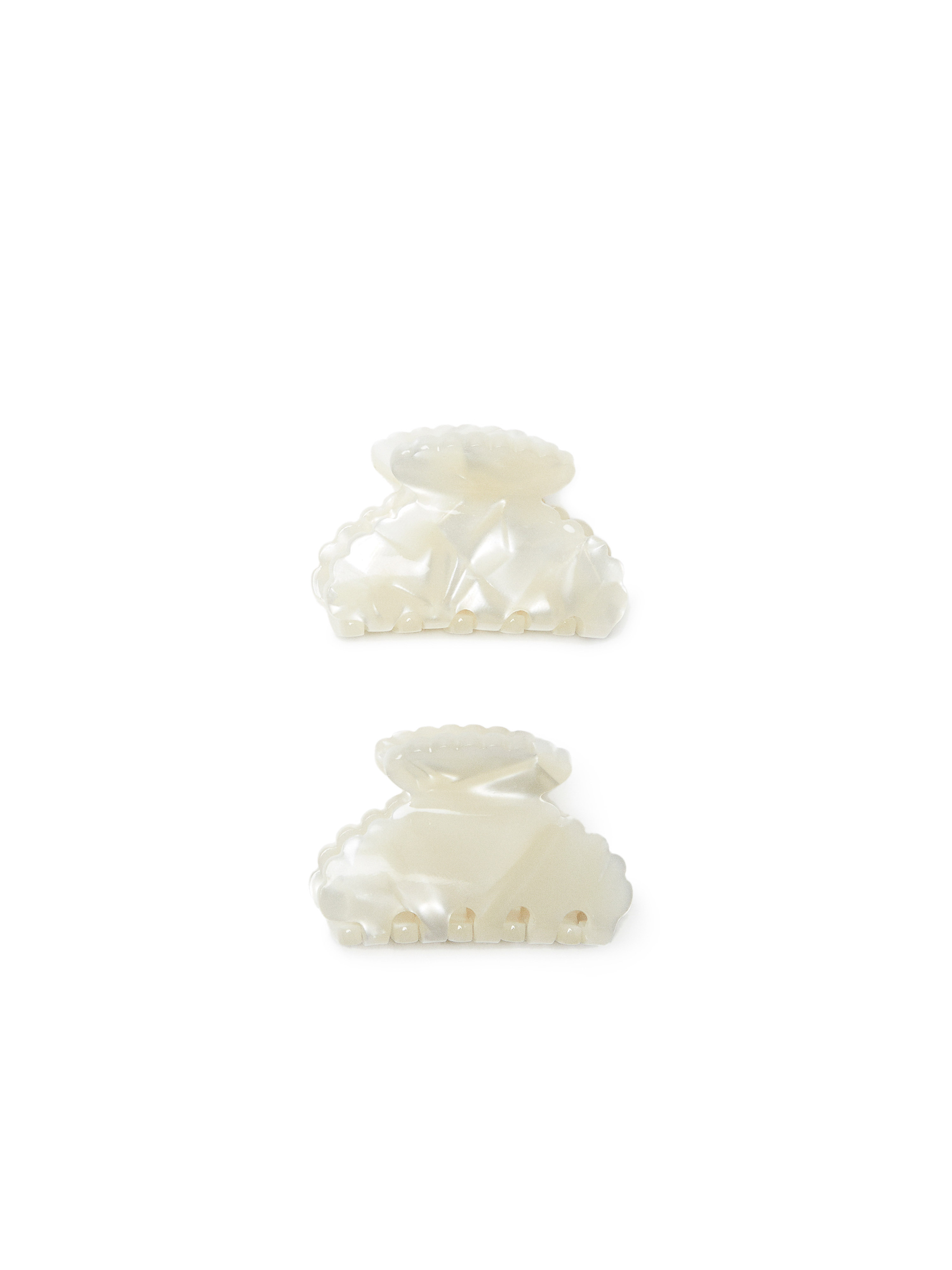 Two off-white hair claw clips are positioned against a bright white backdrop, showcasing their scalloped edges and shiny finish.