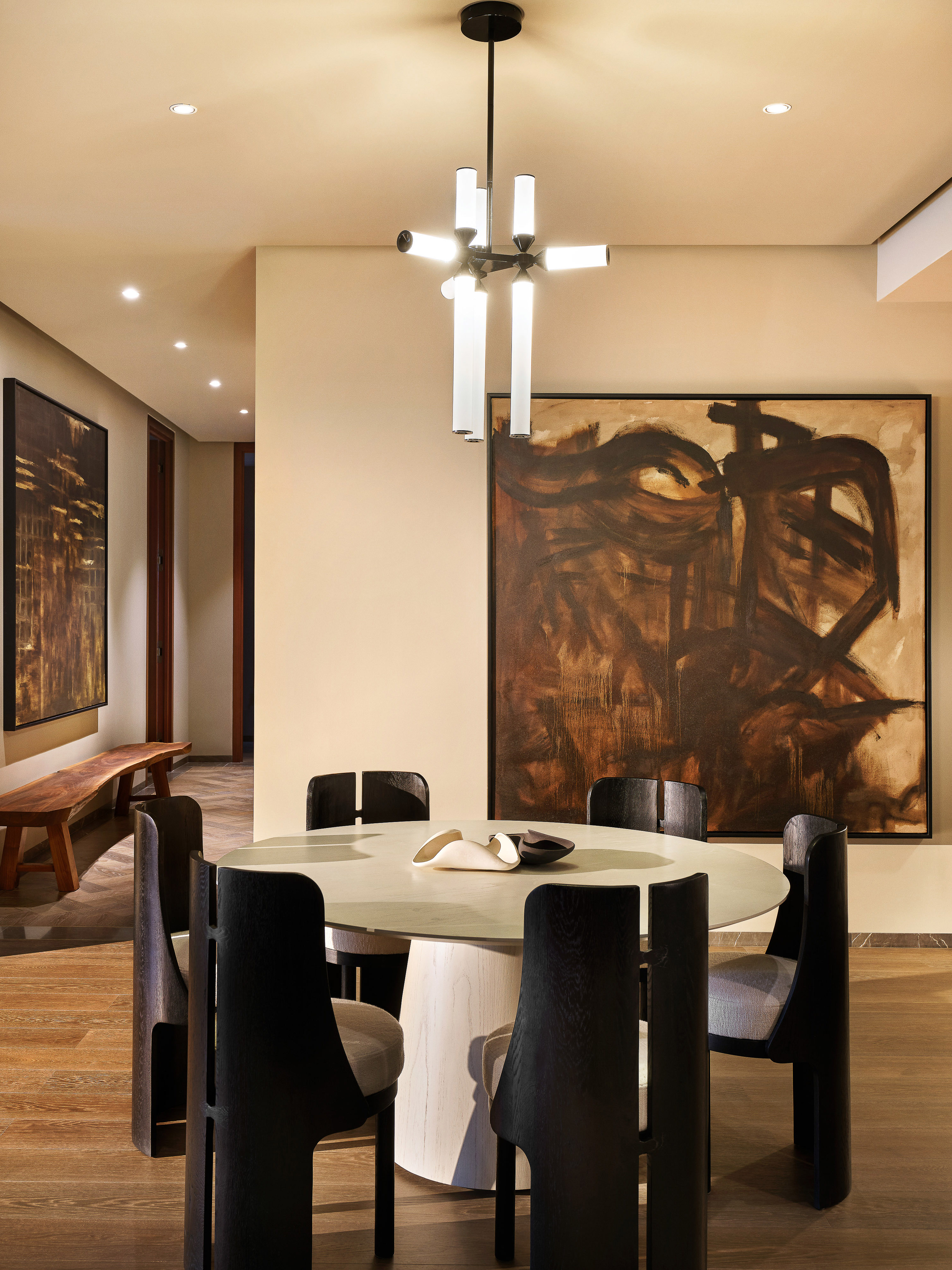 Contemporary dining room with modern chandelier, abstract art, round table and black chairs in a neutral-toned interior space.