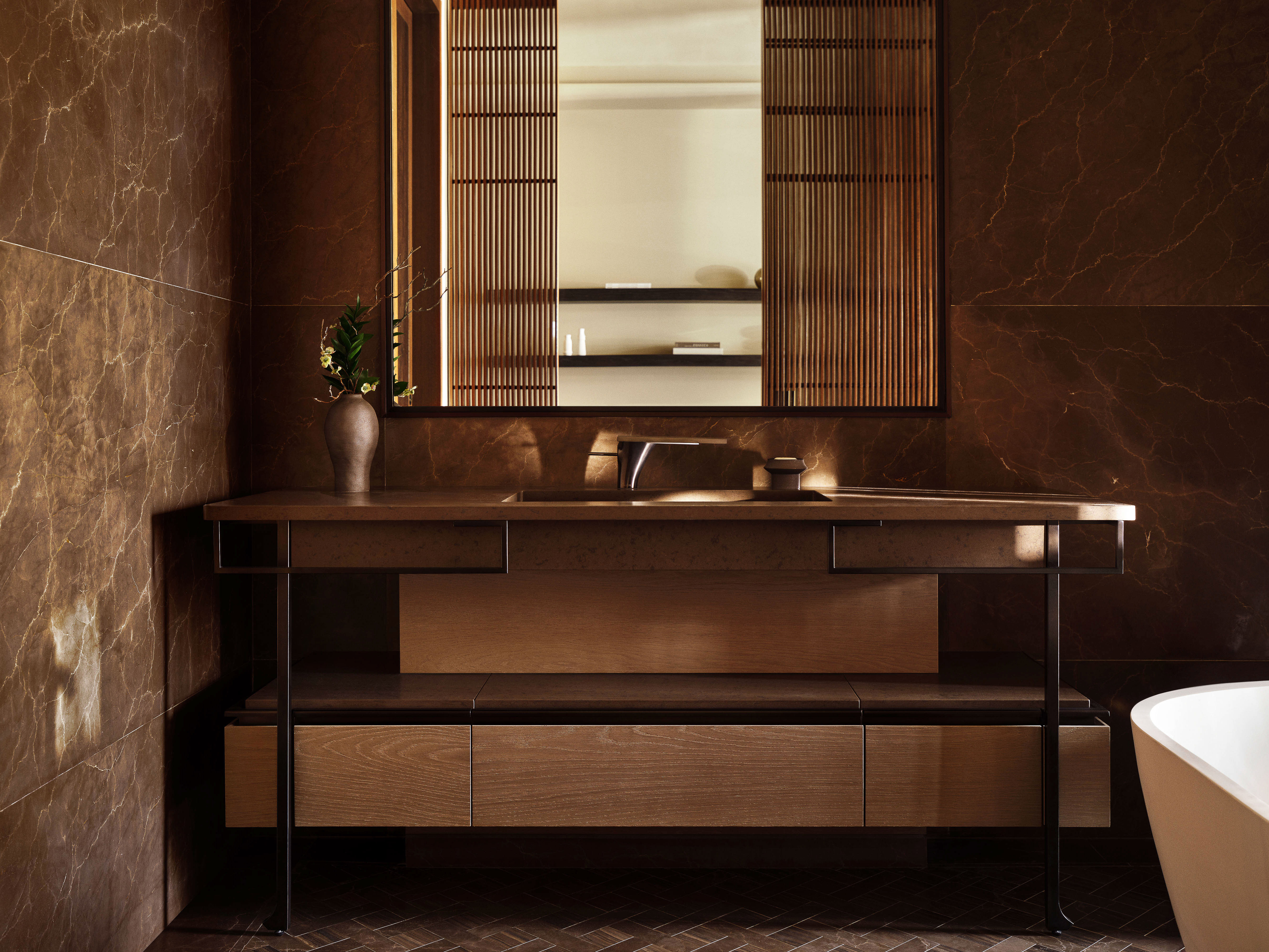 Modern bathroom interior featuring a wood vanity with a decorative vase, a large mirror with wood accents, and marble-like brown tile walls.