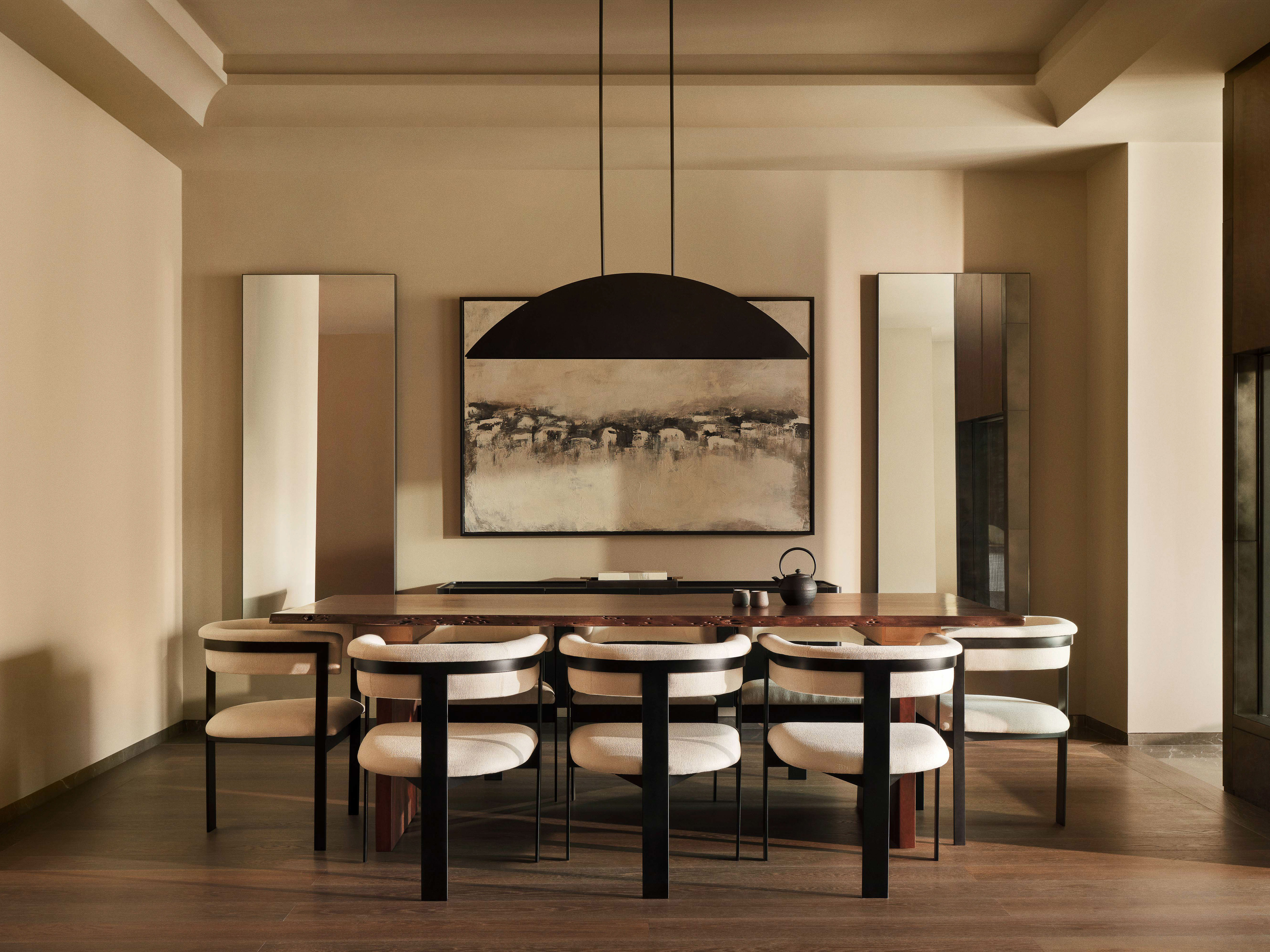 Contemporary dining room interior with wood table, black chairs, and modern abstract art in neutral color palette with warm lighting.