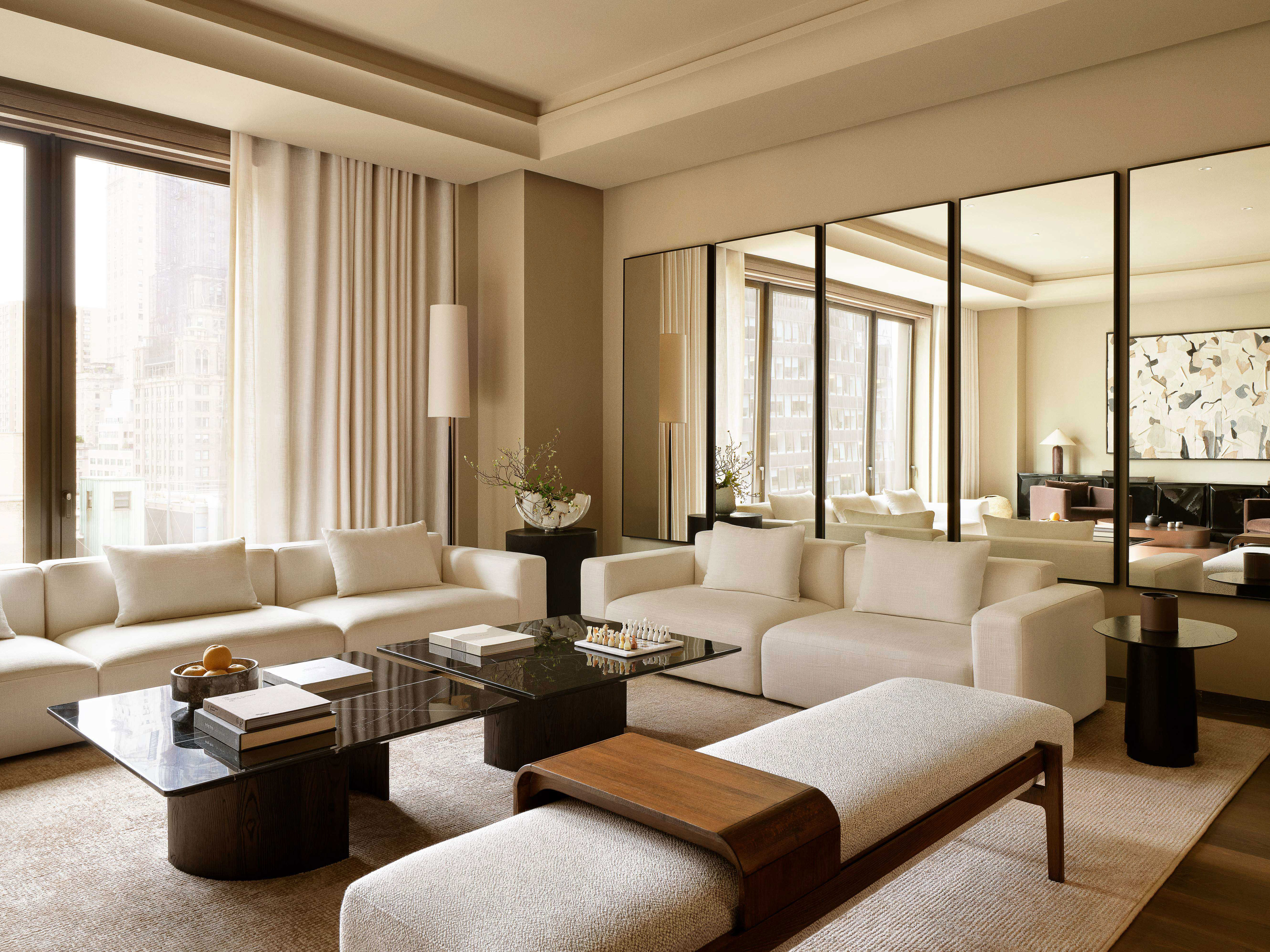 Living room interior featuring white modular sofas, marble coffee tables, and a light gray bench with hardwood trim in a neutral color palette.