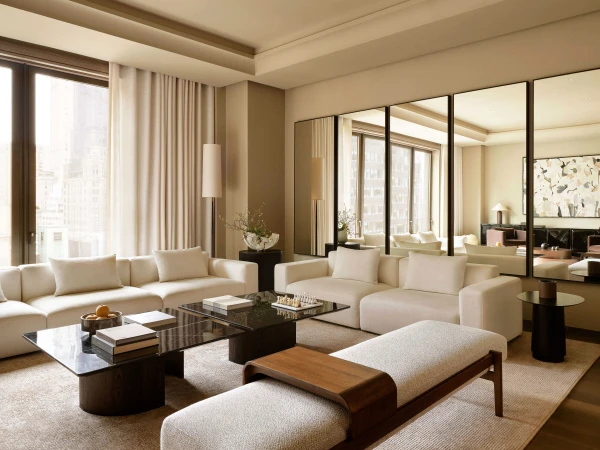 Living room interior featuring white modular sofas, marble coffee tables, and a light gray bench with hardwood trim in a neutral color palette.