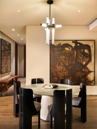 Contemporary dining area with a round table, sculptural black chairs, modern chandelier, and large abstract wall art.