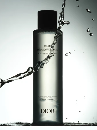 Cosmetic bottle with water splash. Clear glass bottle with black cap and Dior logo against a light background. Beauty shot.