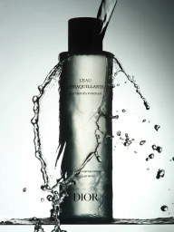 Dior micellar water bottle surrounded by a dynamic frozen splash of water against a backlit studio background.