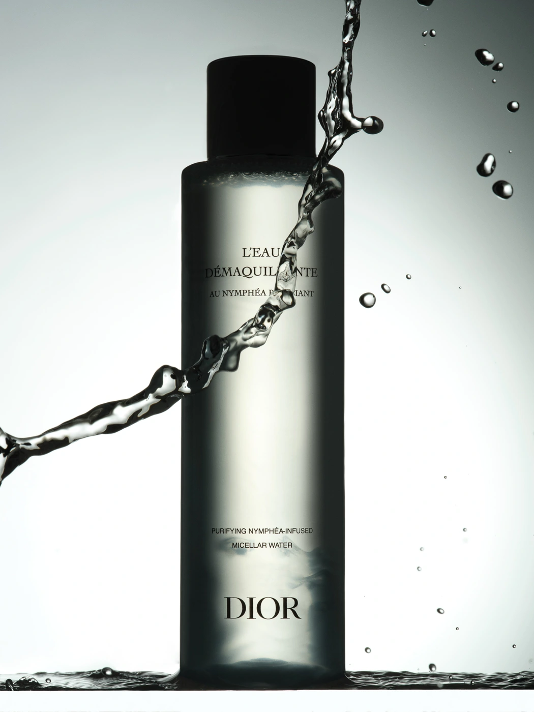Dior micellar water bottle standing in water with dynamic splashing water droplets swirling around against a gradient background.
