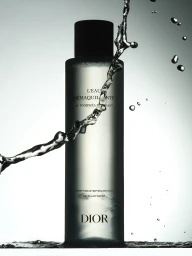 Dior micellar water bottle standing in water with dynamic splashing water droplets swirling around against a gradient background.