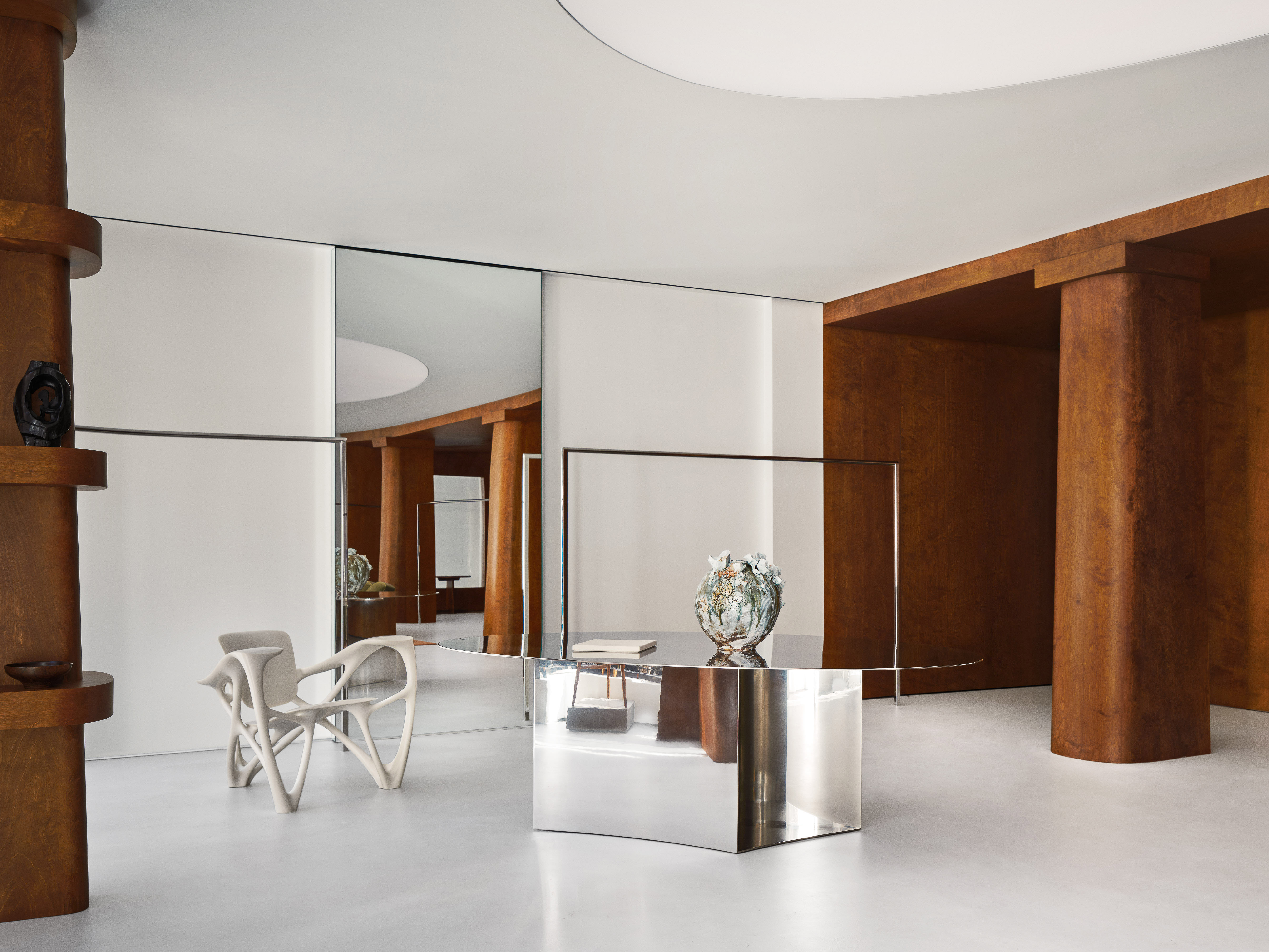 Interior view of a modern showroom featuring an ornate white chair, a mirrored table with a decorative vase, and wood-clad architectural details.